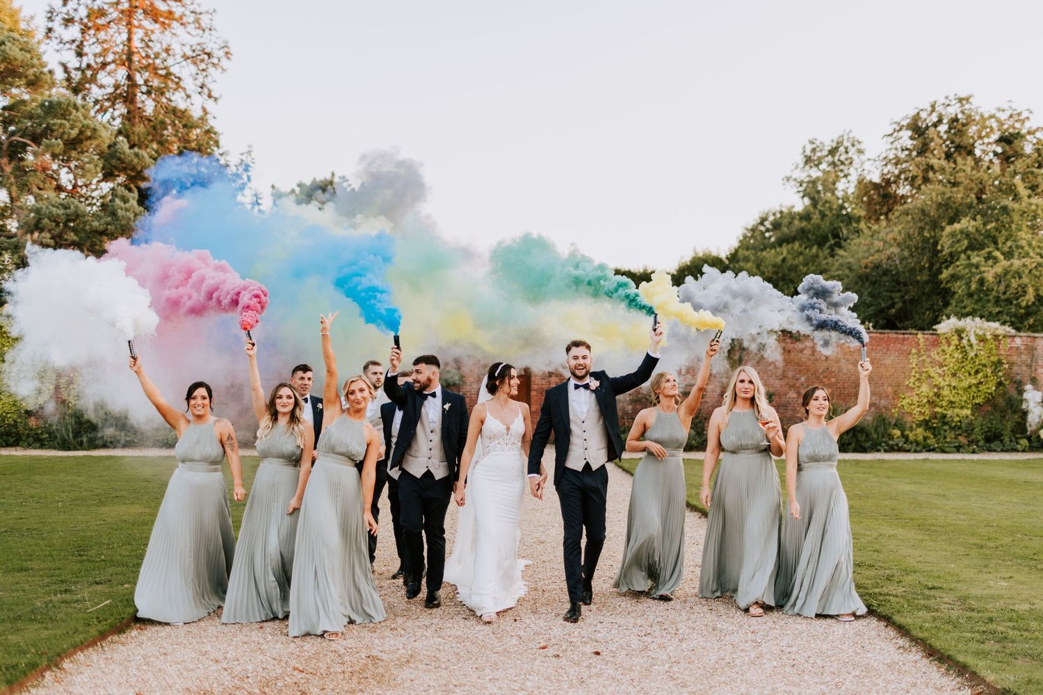 Wedding party celebrates with colorful smoke bombs in an outdoor setting.