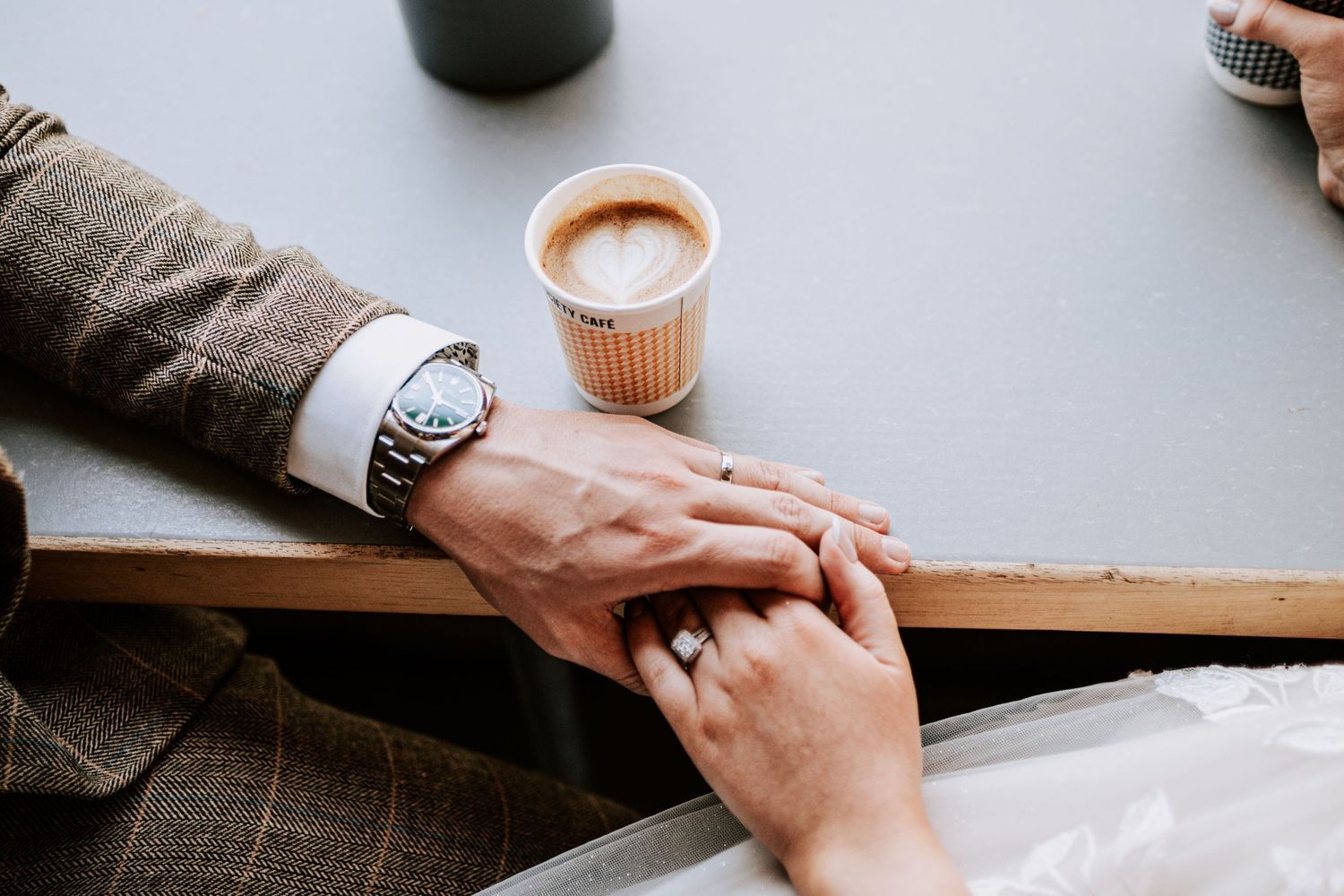 Close-up of hands touching across wooden table with coffee cup in background.