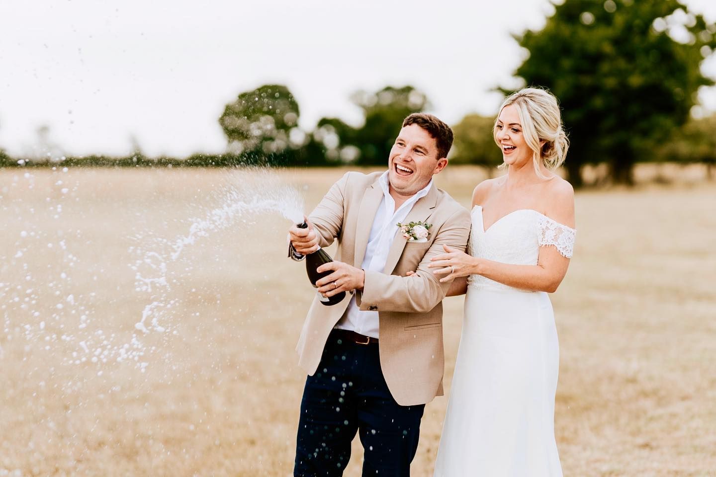 Couple pops champagne in celebration outdoors on their wedding day.