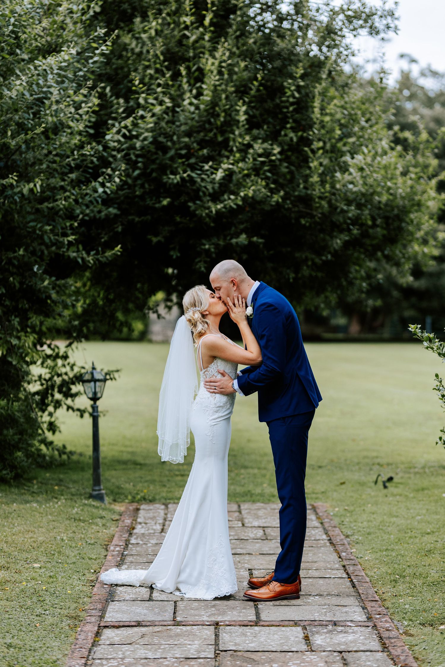 Intimate wedding moment on a garden path surrounded by lush greenery.
