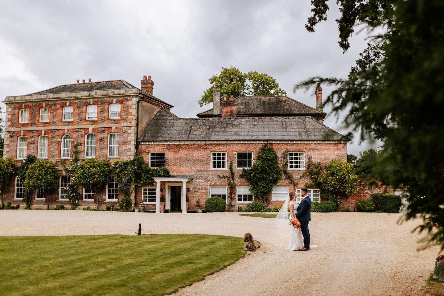 Elegant brick country house with manicured lawn and gravel path on an overcast day.