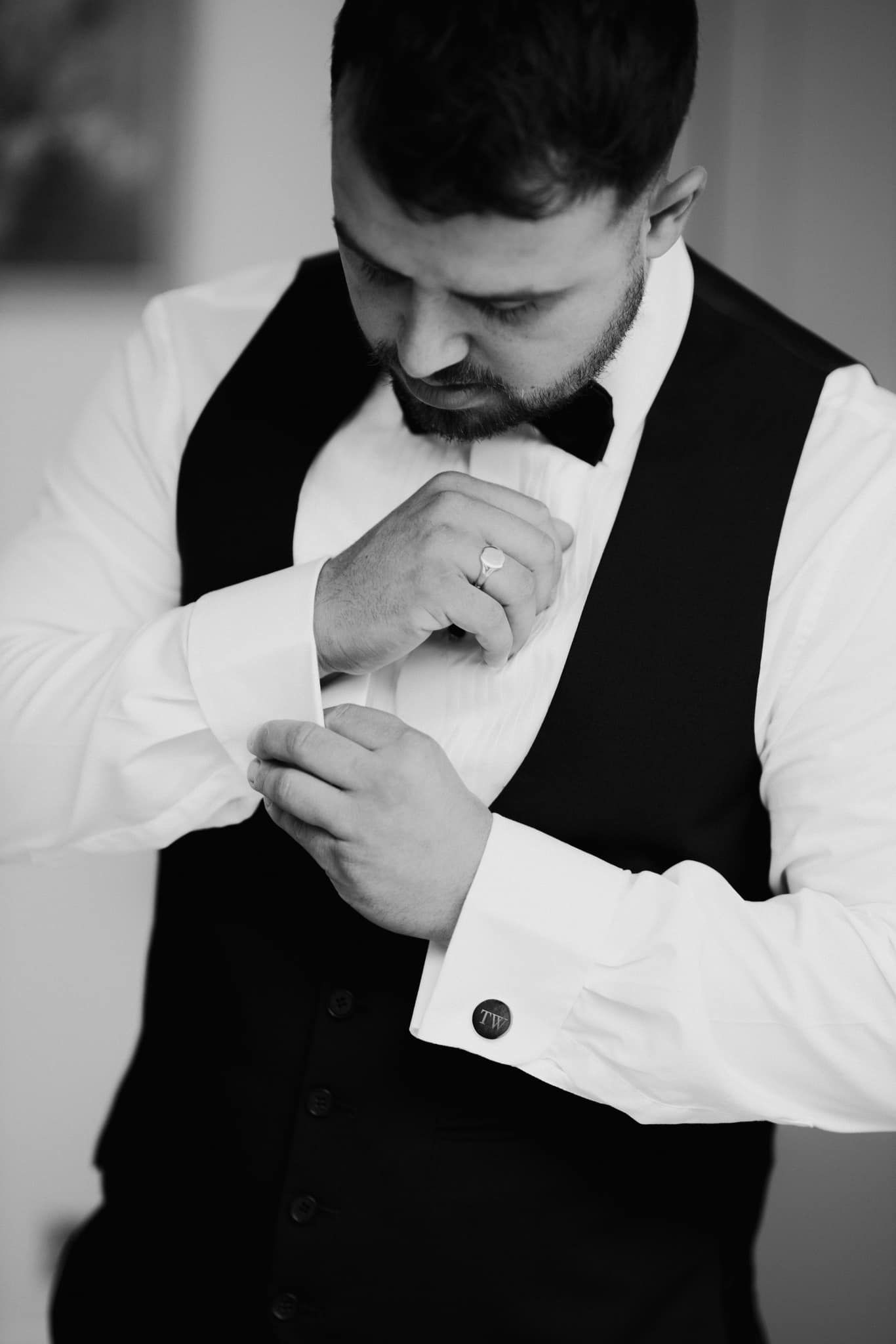 Groom in formal attire adjusting cufflinks in black and white photo.