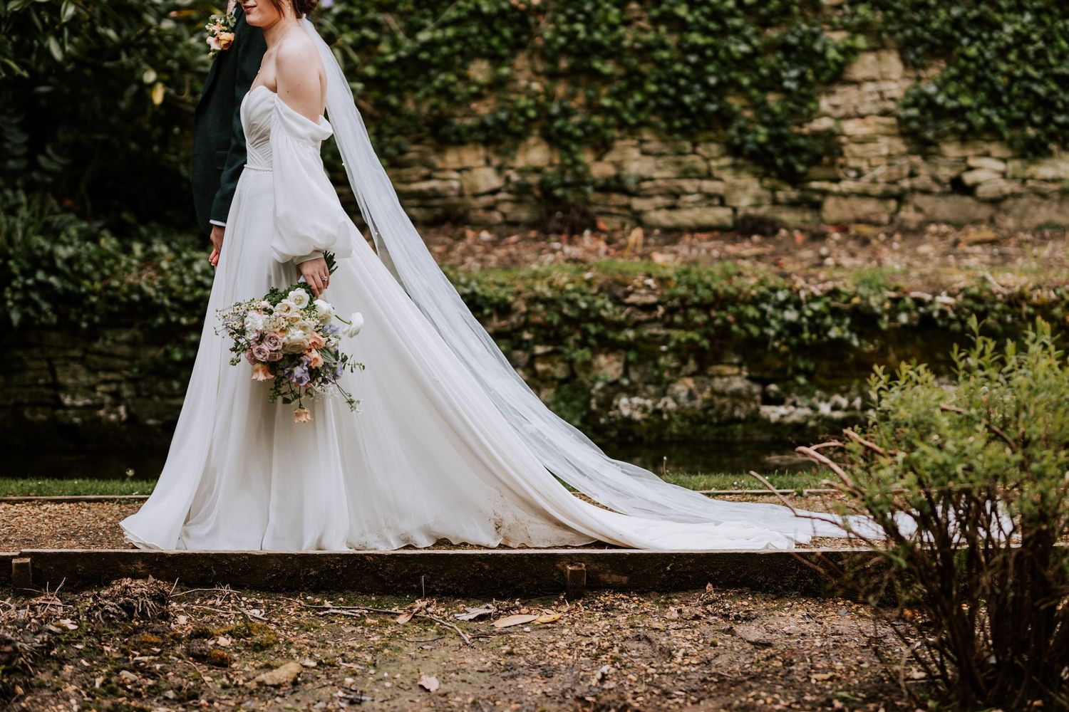 Couple in elegant wedding attire sharing romantic moments along a scenic garden path.