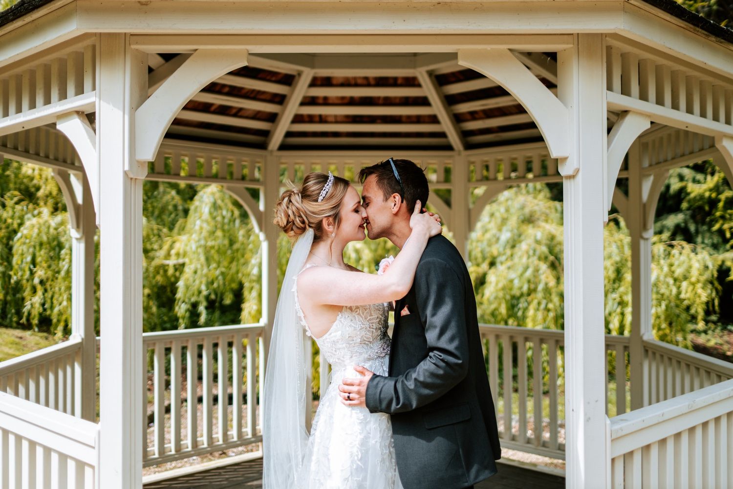 Wedding ceremony taking place under a white wooden gazebo.