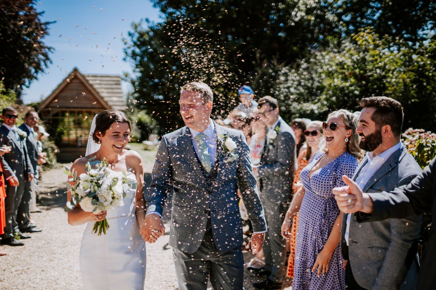 Wedding celebration with confetti throw outside rustic venue on sunny day.