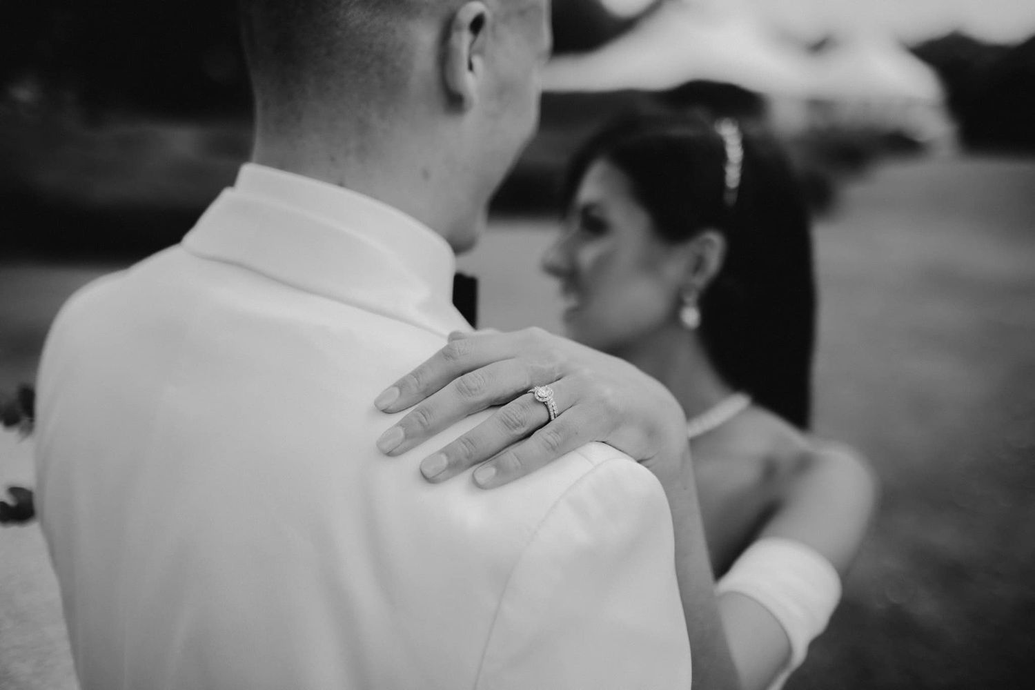 A black and white close-up photograph showing a hand resting on a shoulder during a wedding moment.