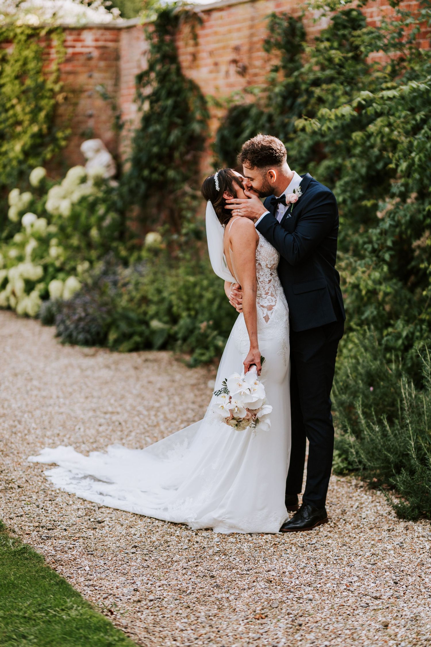 Romantic garden wedding portraits along a rustic brick wall with trailing vines and flowers.
