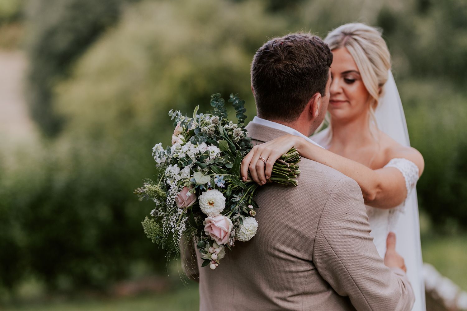 Romantic sunset portrait of couple embracing with pink and white floral bouquet.