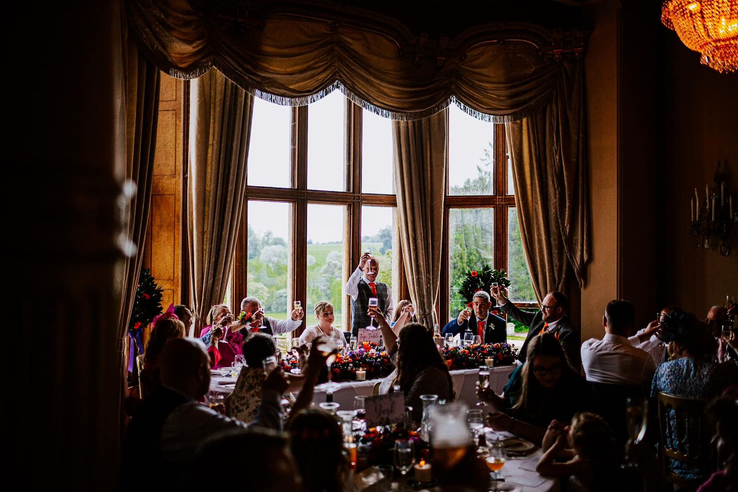 Wedding reception venue with elegant drapes and chandelier filled with celebrating guests.