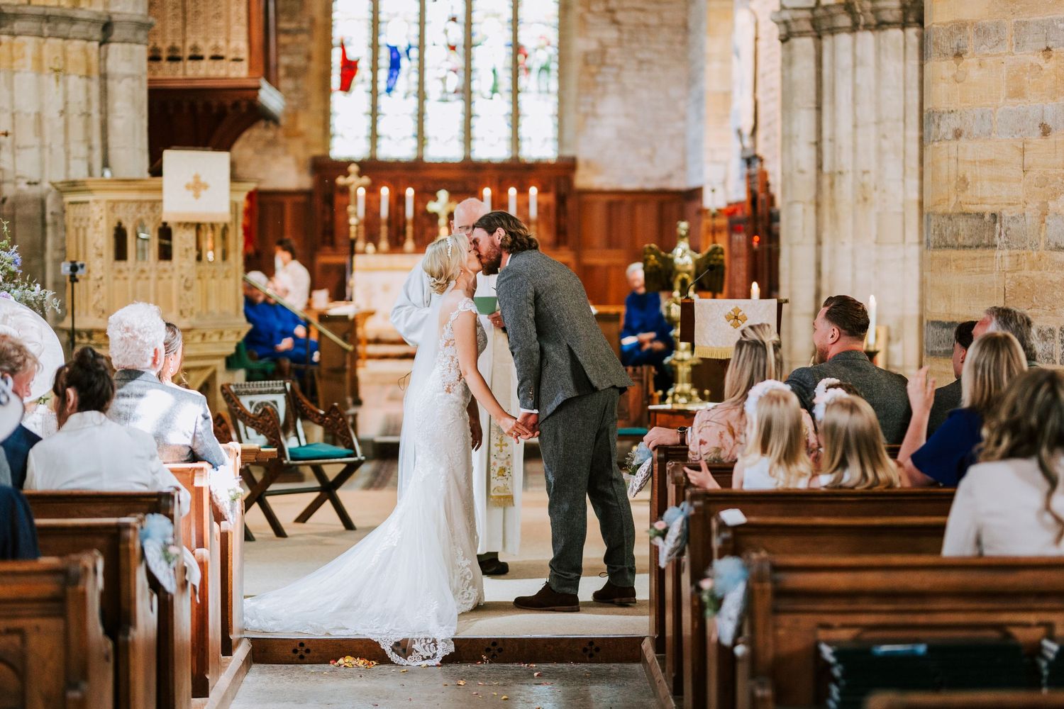 Traditional church ceremony with guests seated in wooden pews during wedding vows.