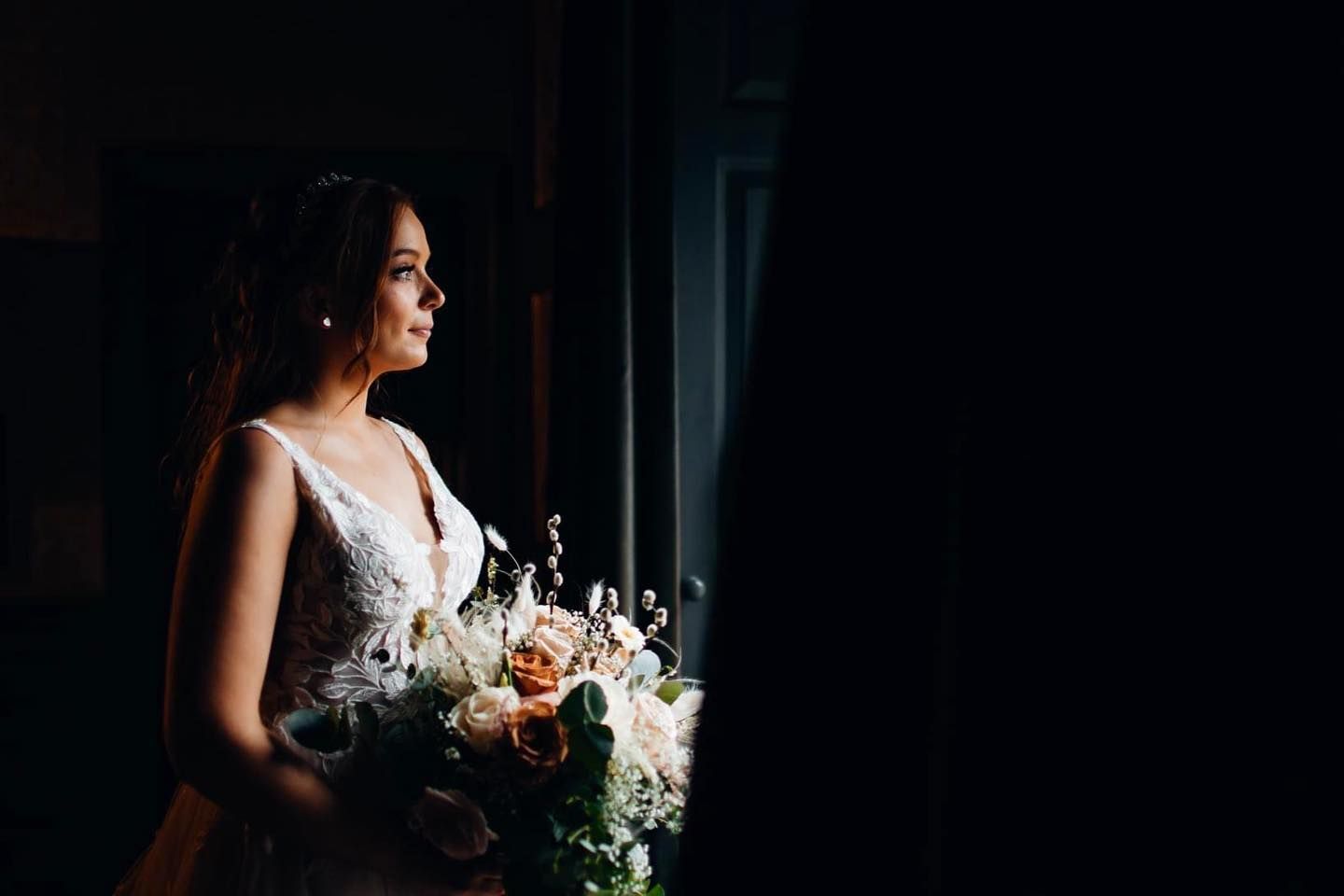 Bride holding bouquet silhouetted against dramatic window light.