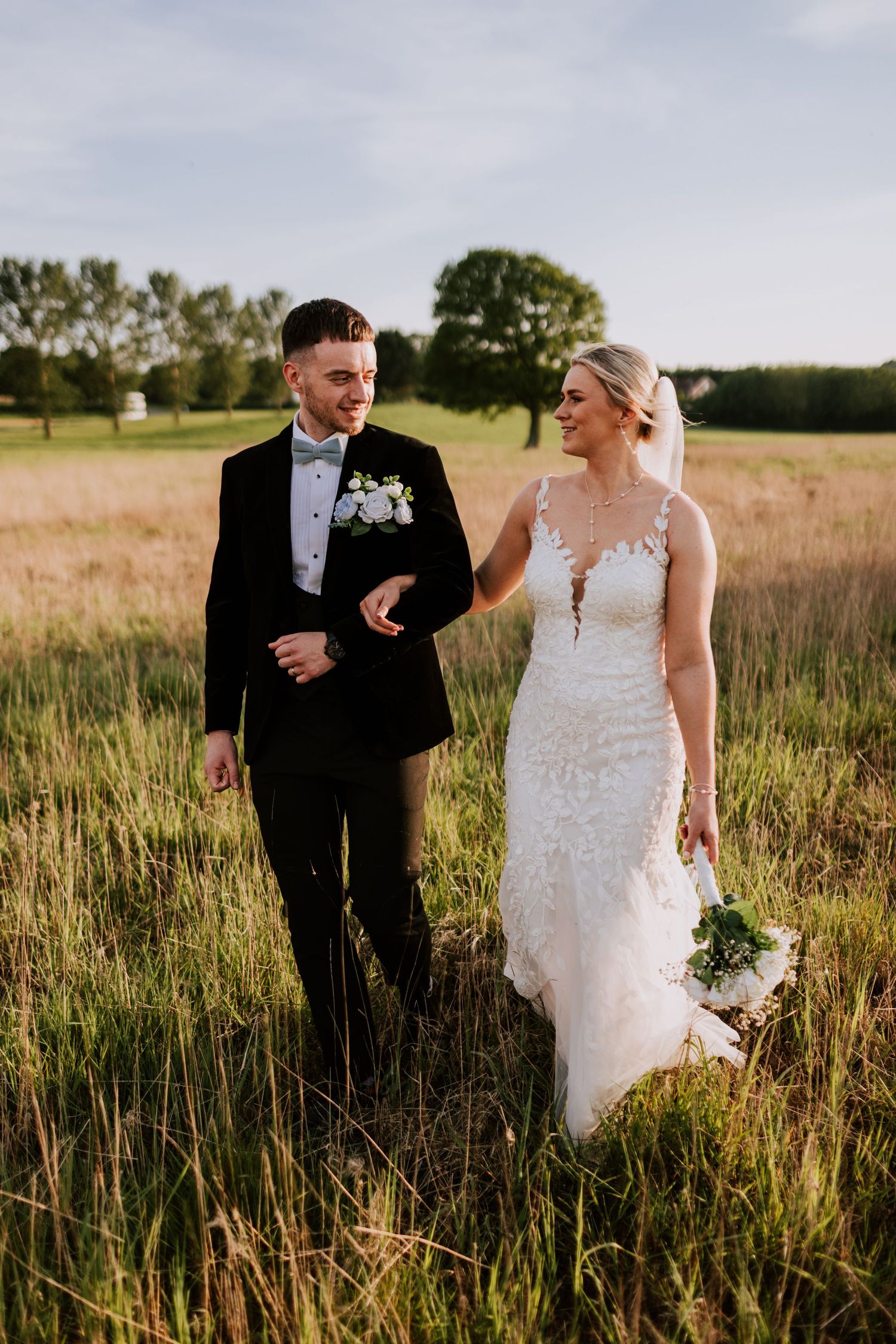 Newlyweds share a romantic moment together in a golden field at sunset.