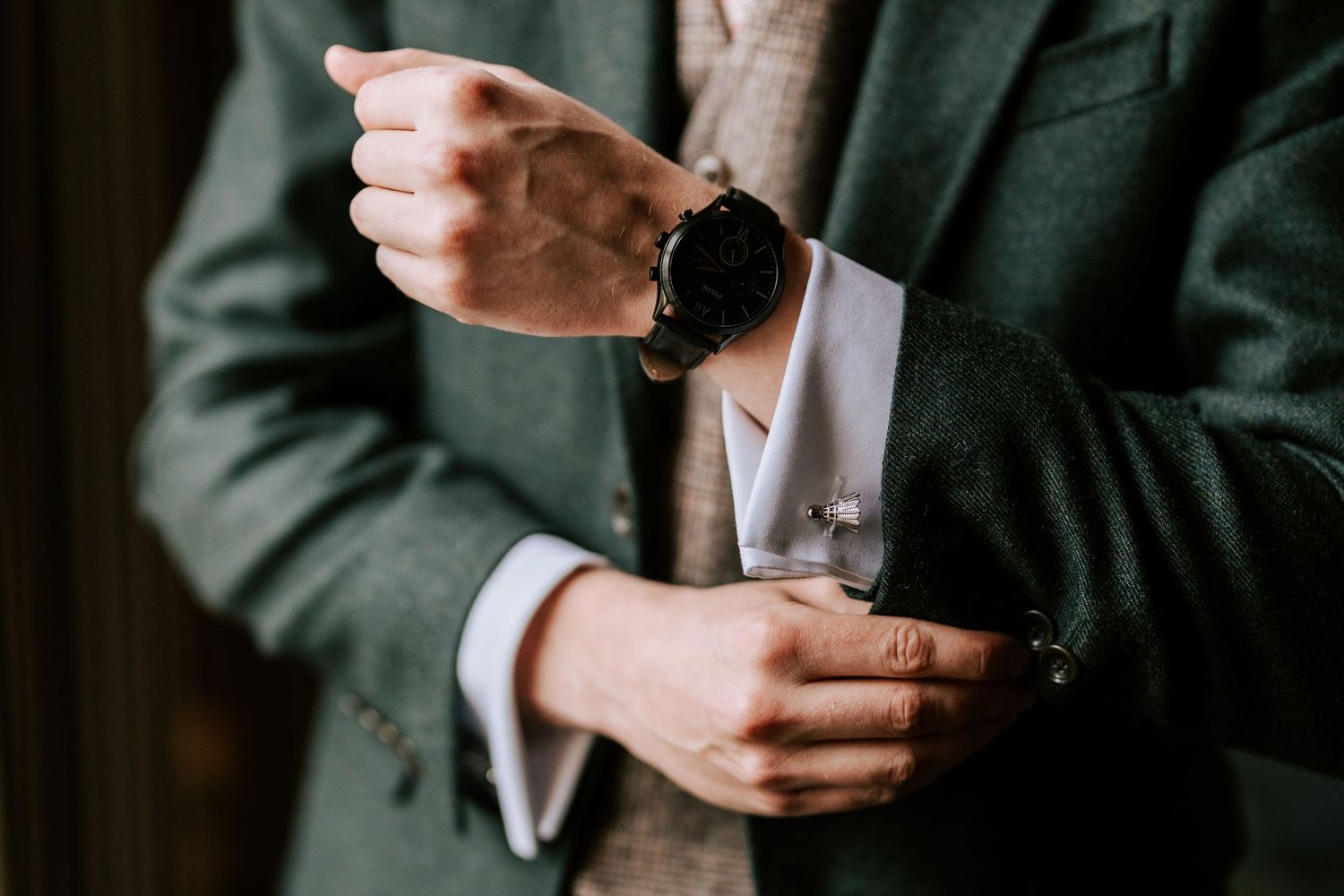 Close-up details of groom's hands and formal attire during wedding preparation.