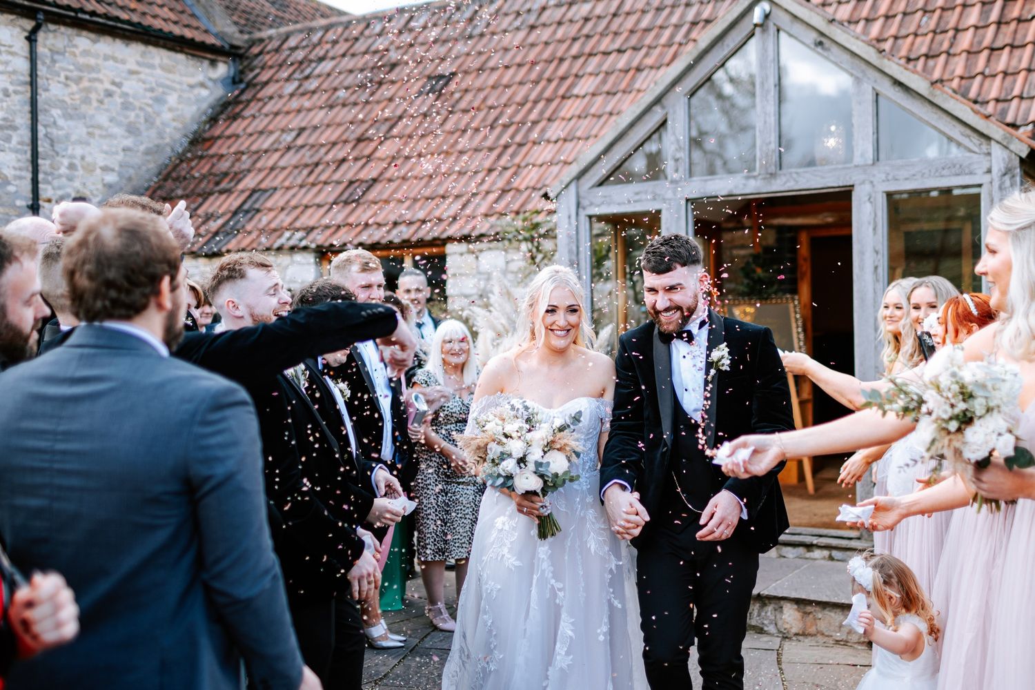 Newlyweds exit stone venue while guests shower them with confetti in celebration.