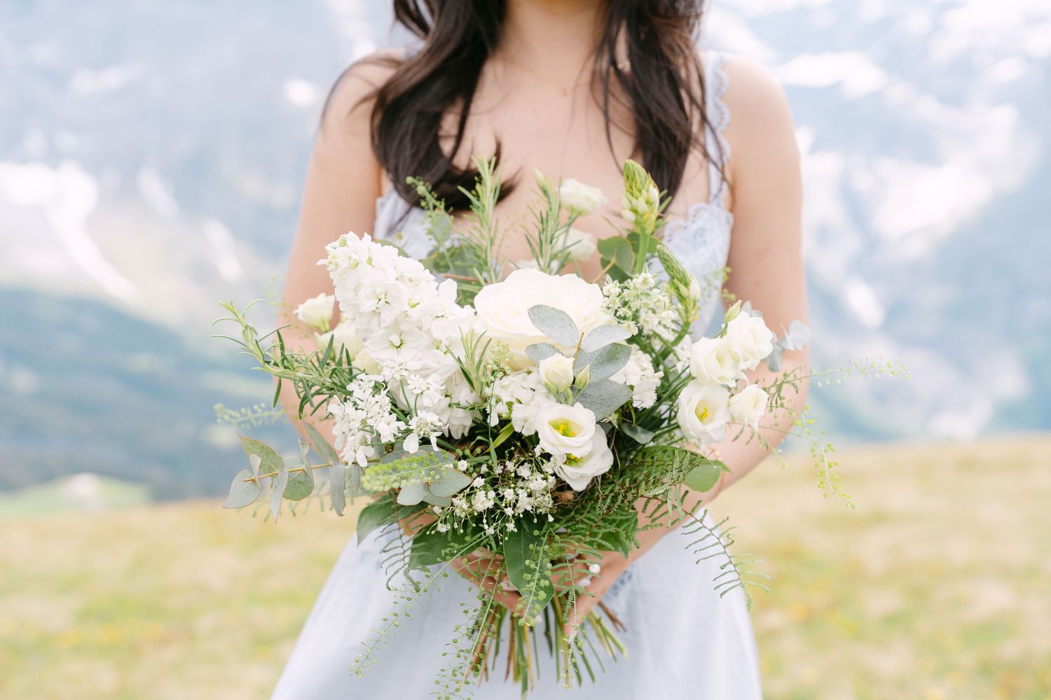 Bride holding a lush white wedding bouquet with greenery, set against a scenic mountain backdrop.
