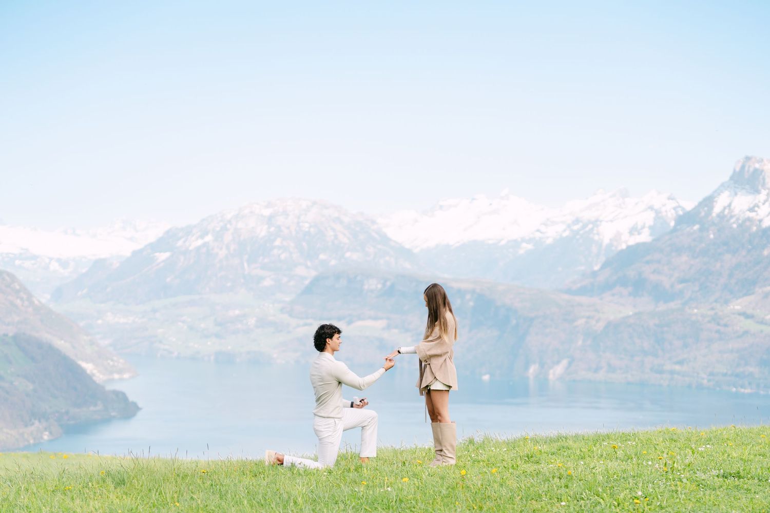 A romantic marriage proposal on a green hillside with stunning Swiss Alps and lake backdrop.