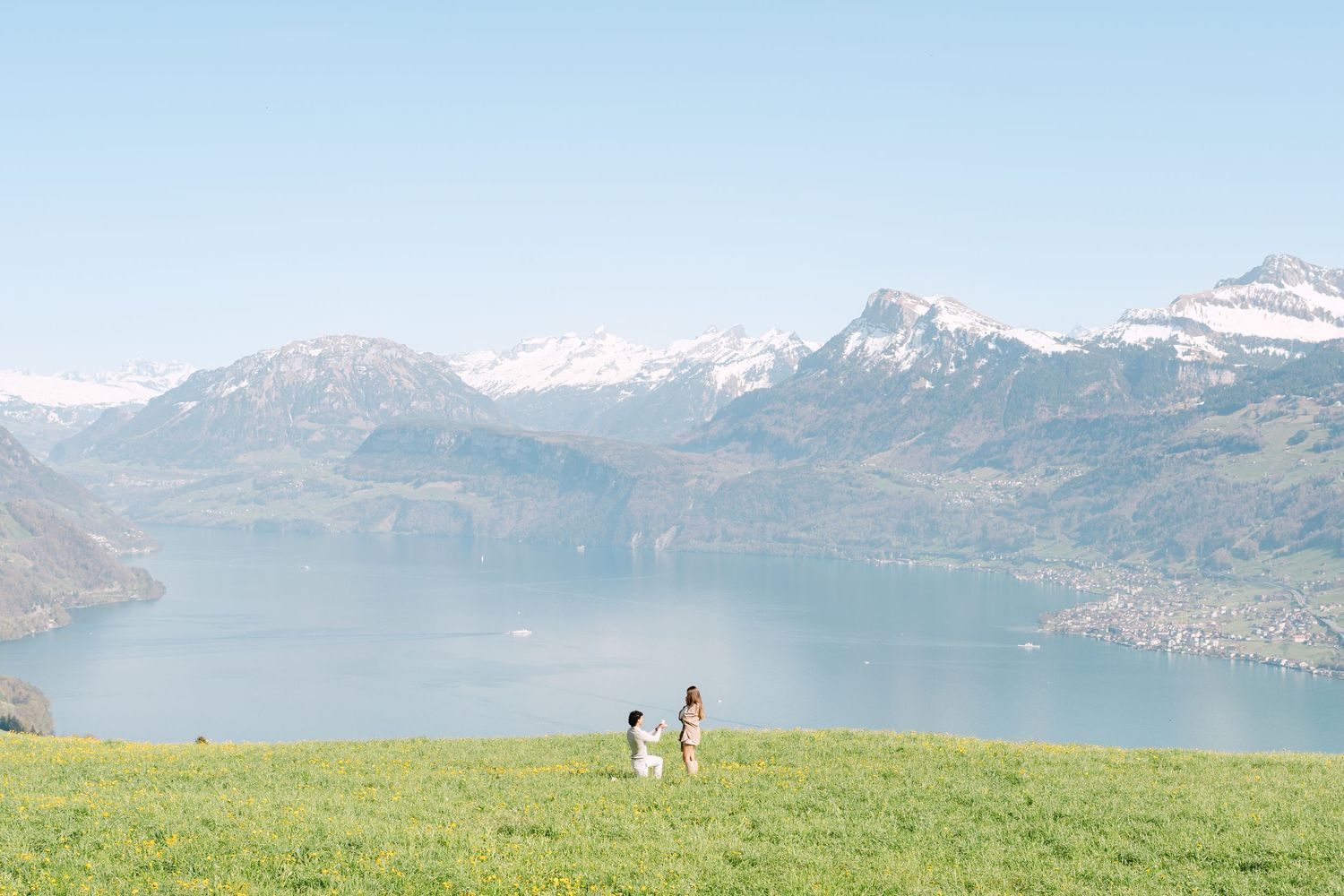 Couple walking on green hillside overlooking Lake Lucerne with snow-capped Swiss Alps in background.