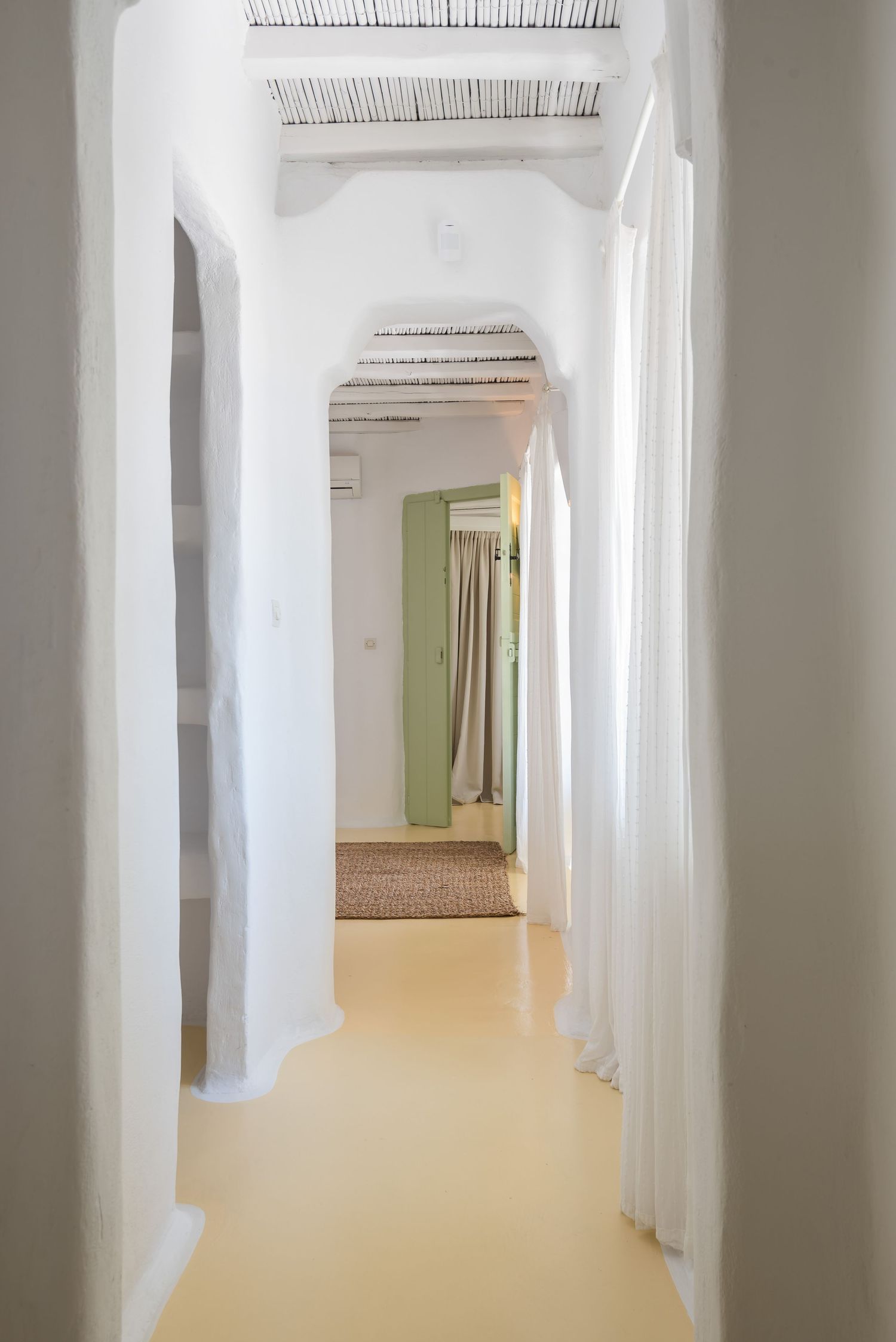 Long white corridor with rustic wooden beams and a mint green curtain visible at the end.