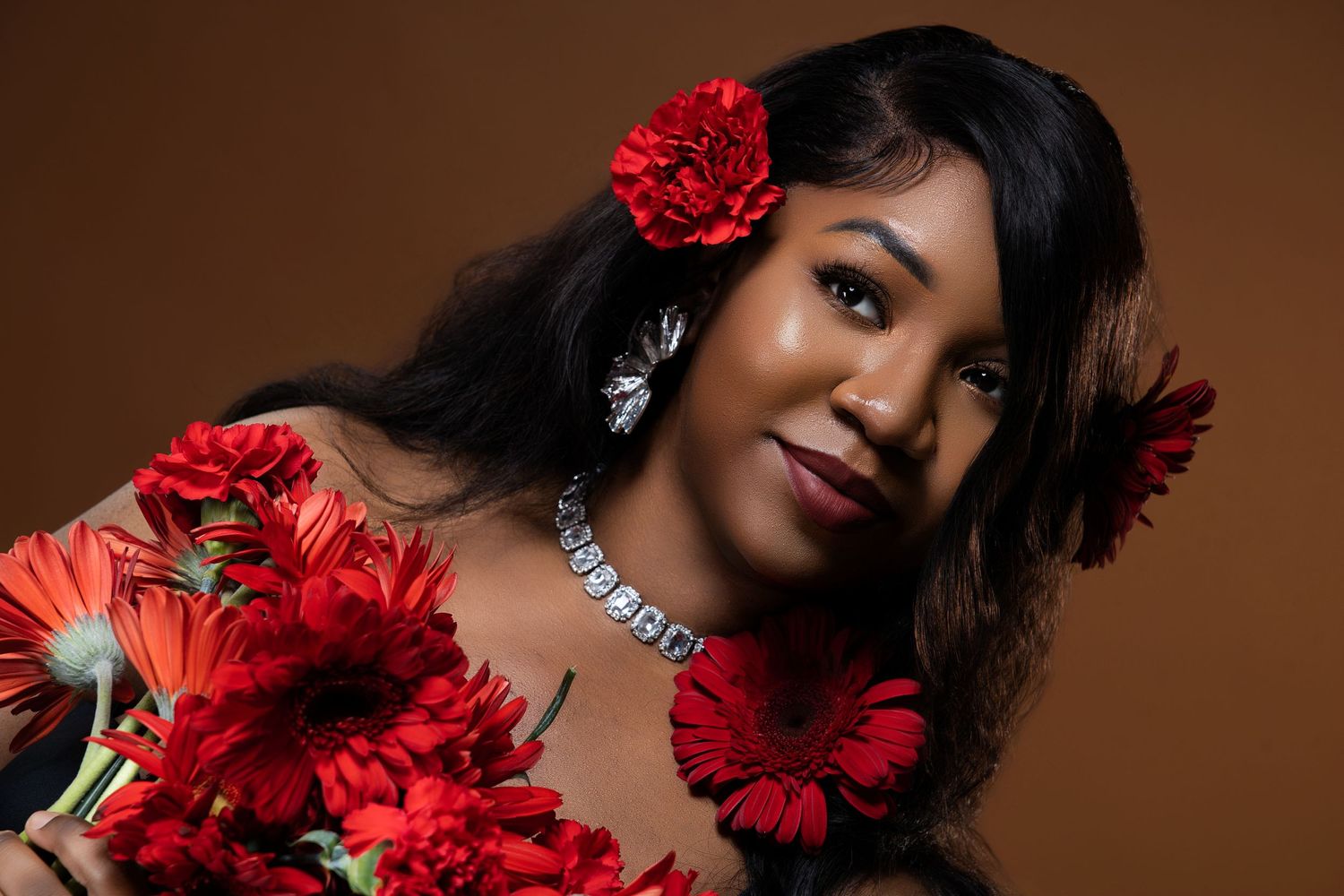 Elegant portrait with red carnations and statement necklace against warm brown backdrop.