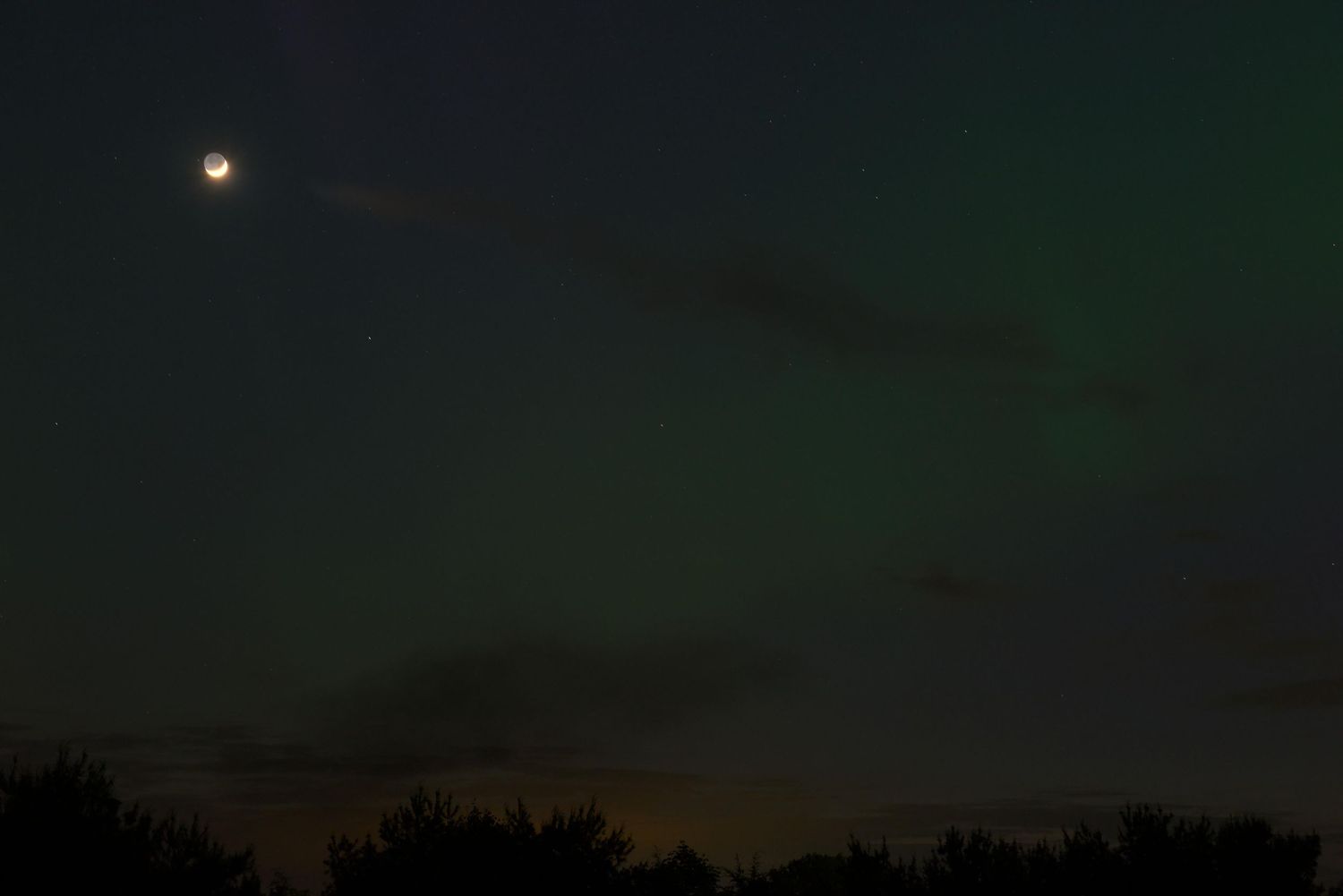 Moonlight illuminates the northern lights seen in Ohio on May 10th 2024. Purple and red swirls dance in the night sky.