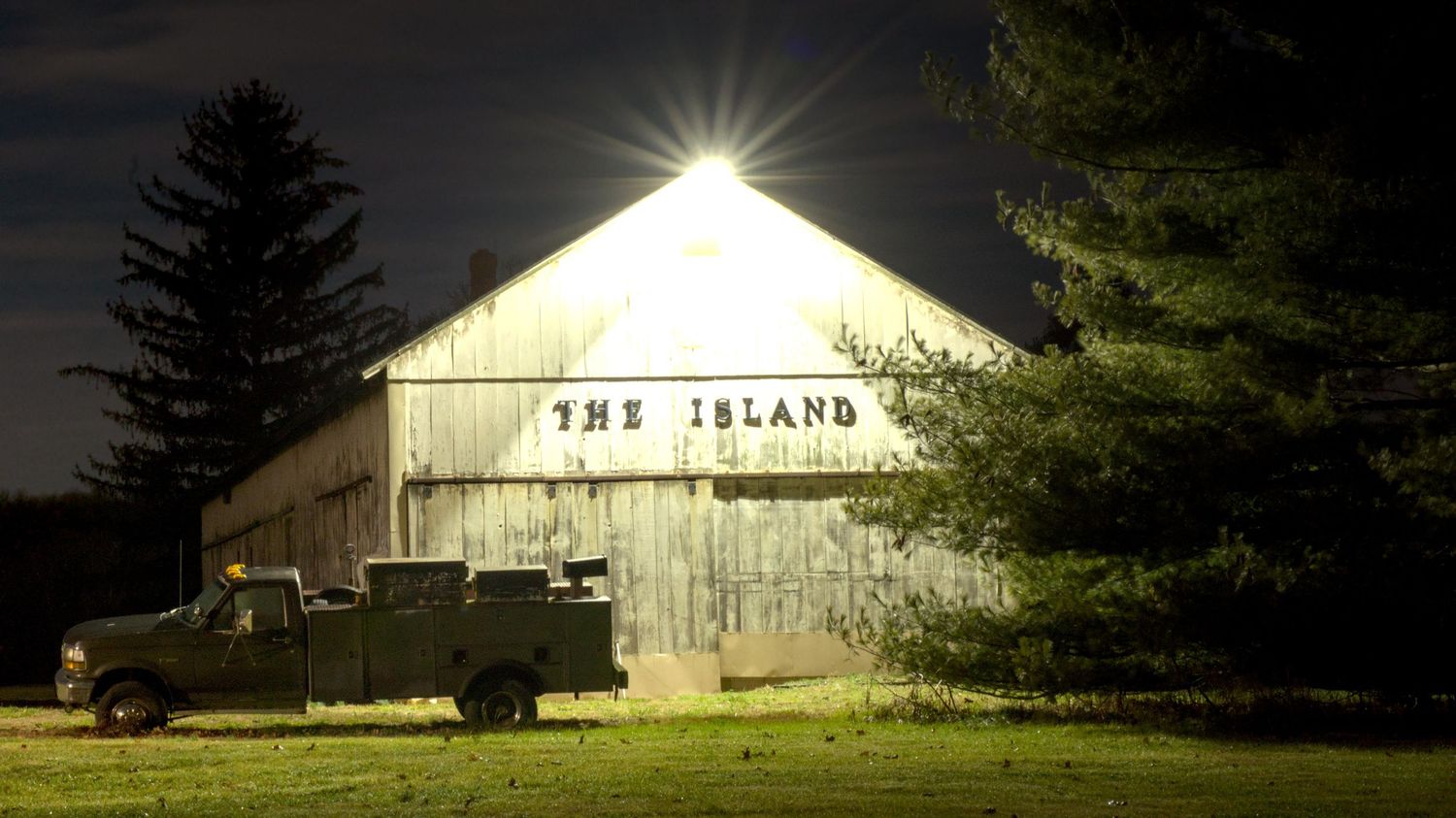 A night time image of a white barn with peeling paint with lettering naming it 