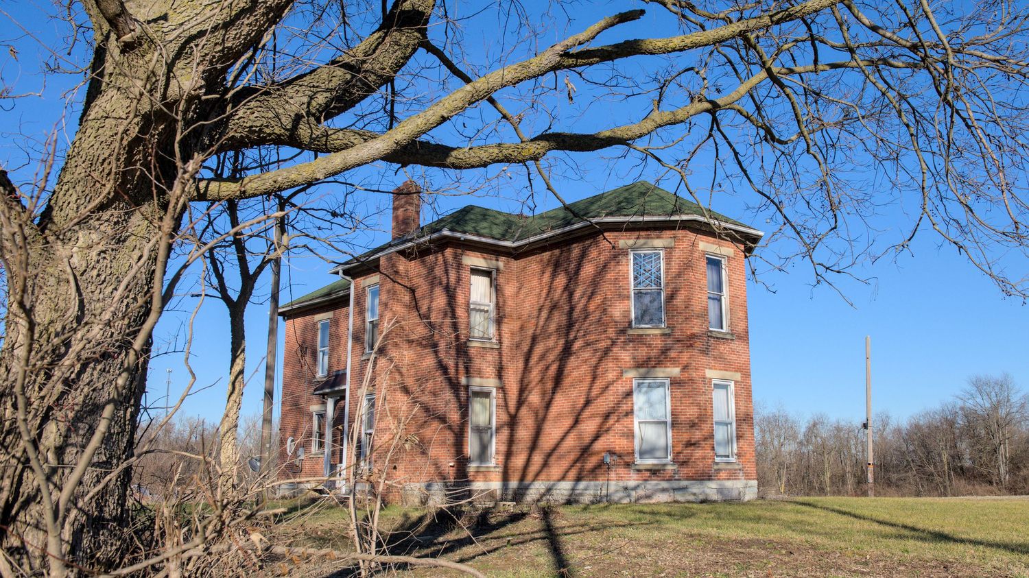 An abandoned brick house stands out from the blue sky with blue painter's tape holding one broken window together.