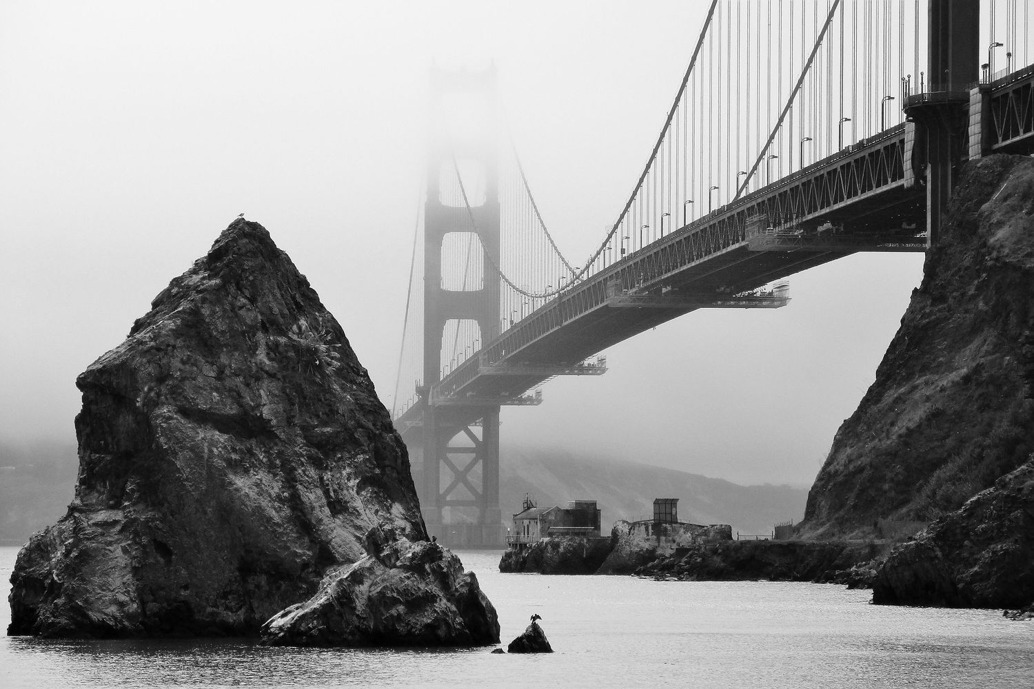 A black and white view of a large boulder in front of the Golden Gate Bridge in San, Francisco, CA. An uncommon view for such common bridge