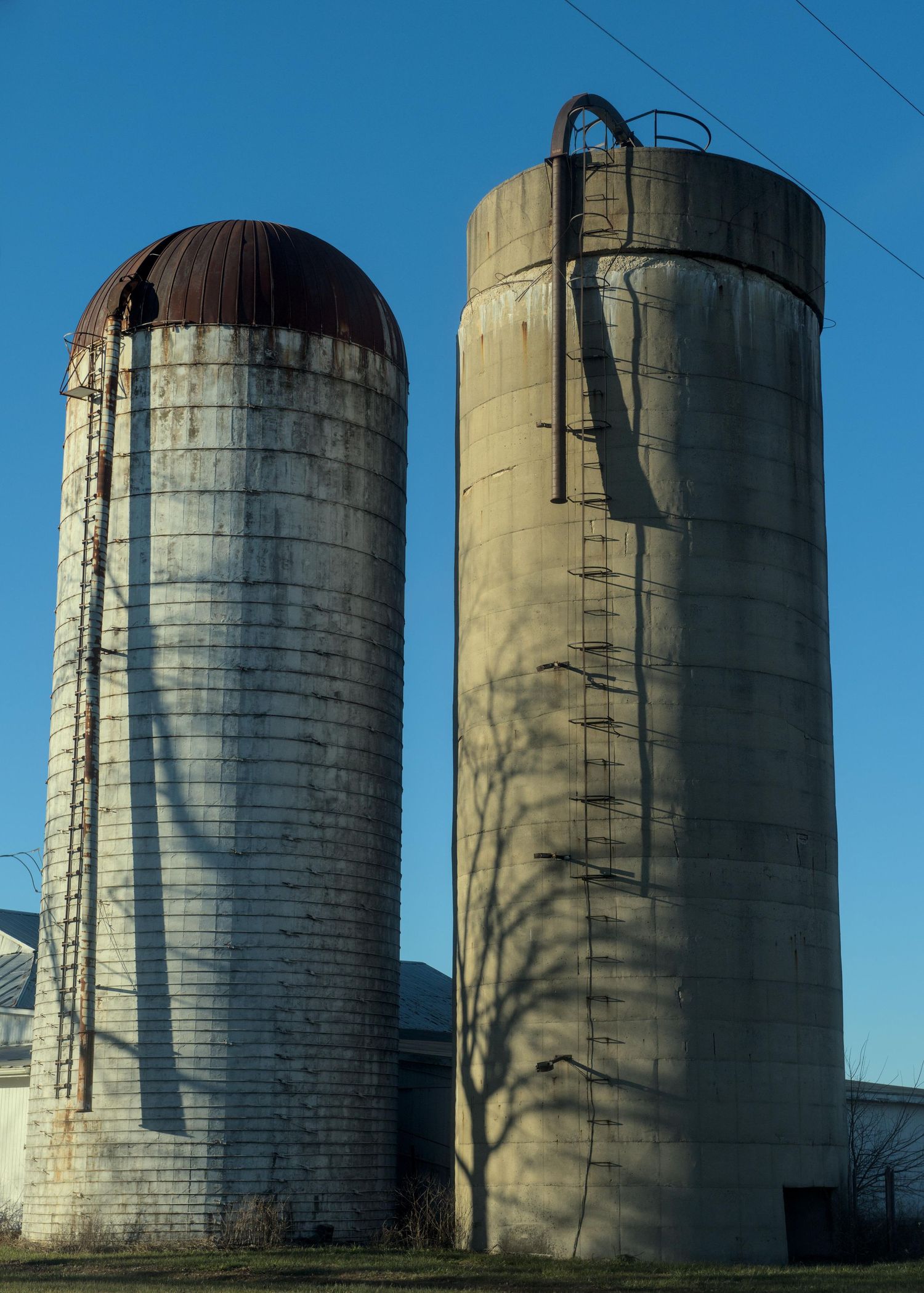 A image depicting two weathered silos with long shadows cascading on them from the ladders that climb up their sides.