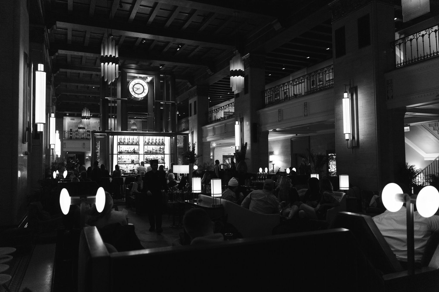 Black-and-white photograph of an elegant Toronto hotel lounge with a large clock, illuminated bar, and guests gathered Royal York Hotel.
