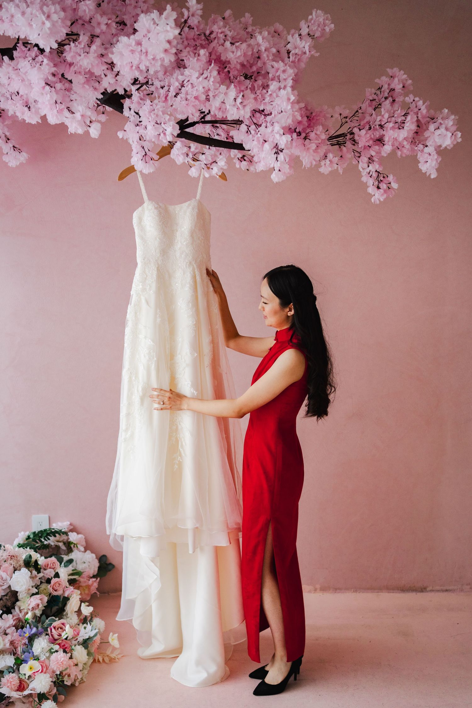 Woman in a red outfit adjusting a wedding dress beneath pink cherry blossom decorations at ESpace Studios.