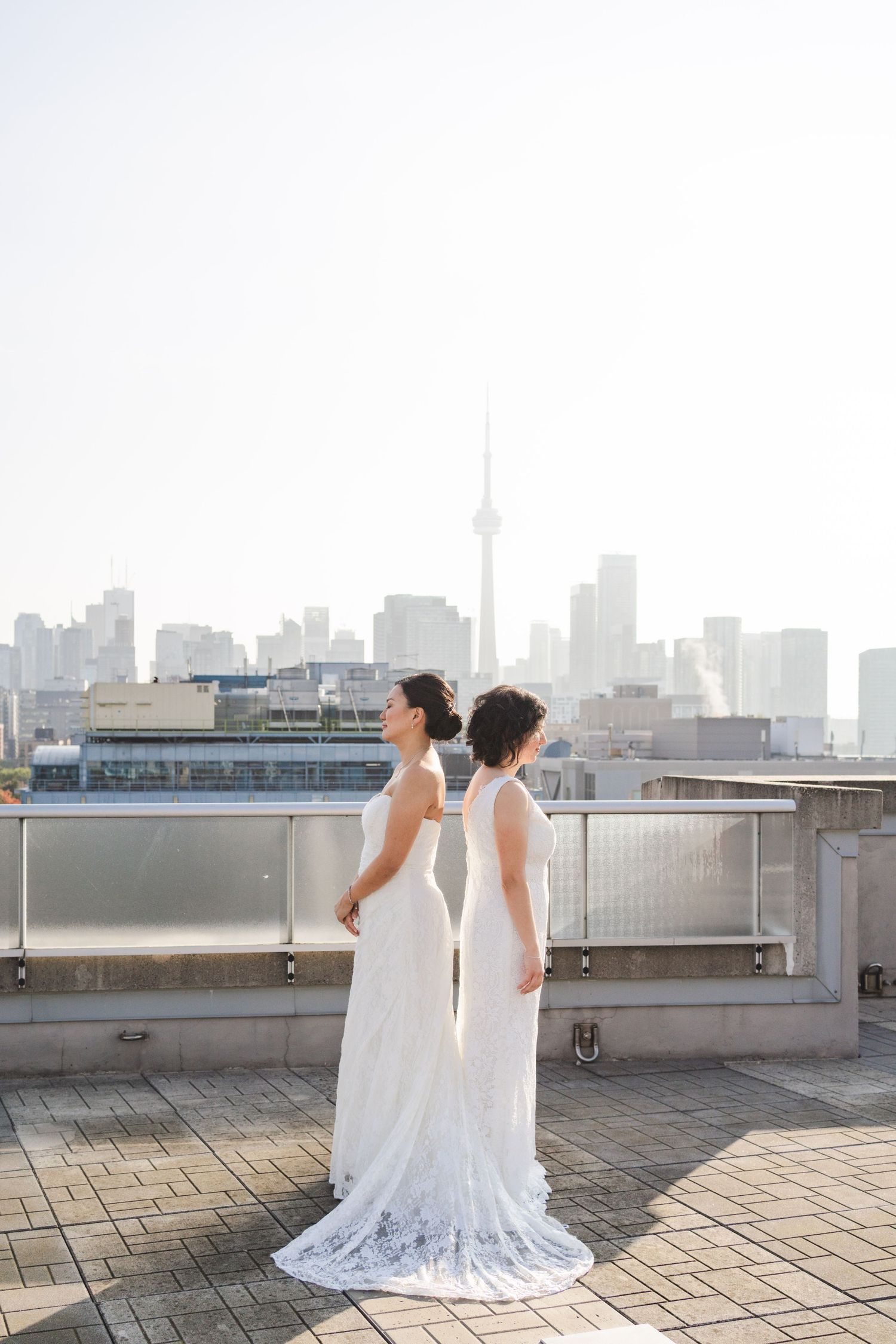 Bride in a white wedding gown standing on a rooftop terrace overlooking the Toronto skyline and CN Tower.