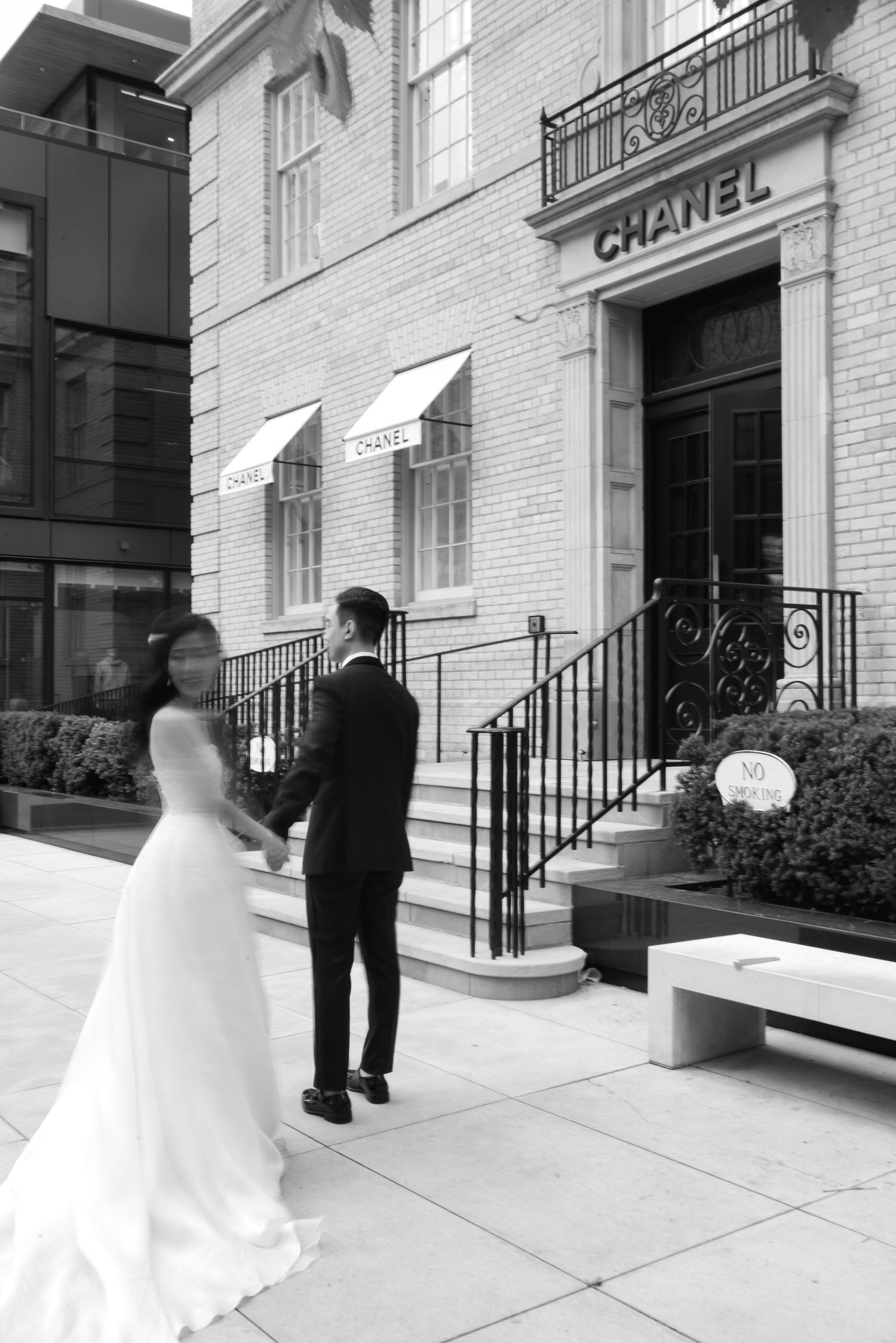 Black-and-white portrait of a bride and groom standing outside an ornate stone building with grand architectural details.