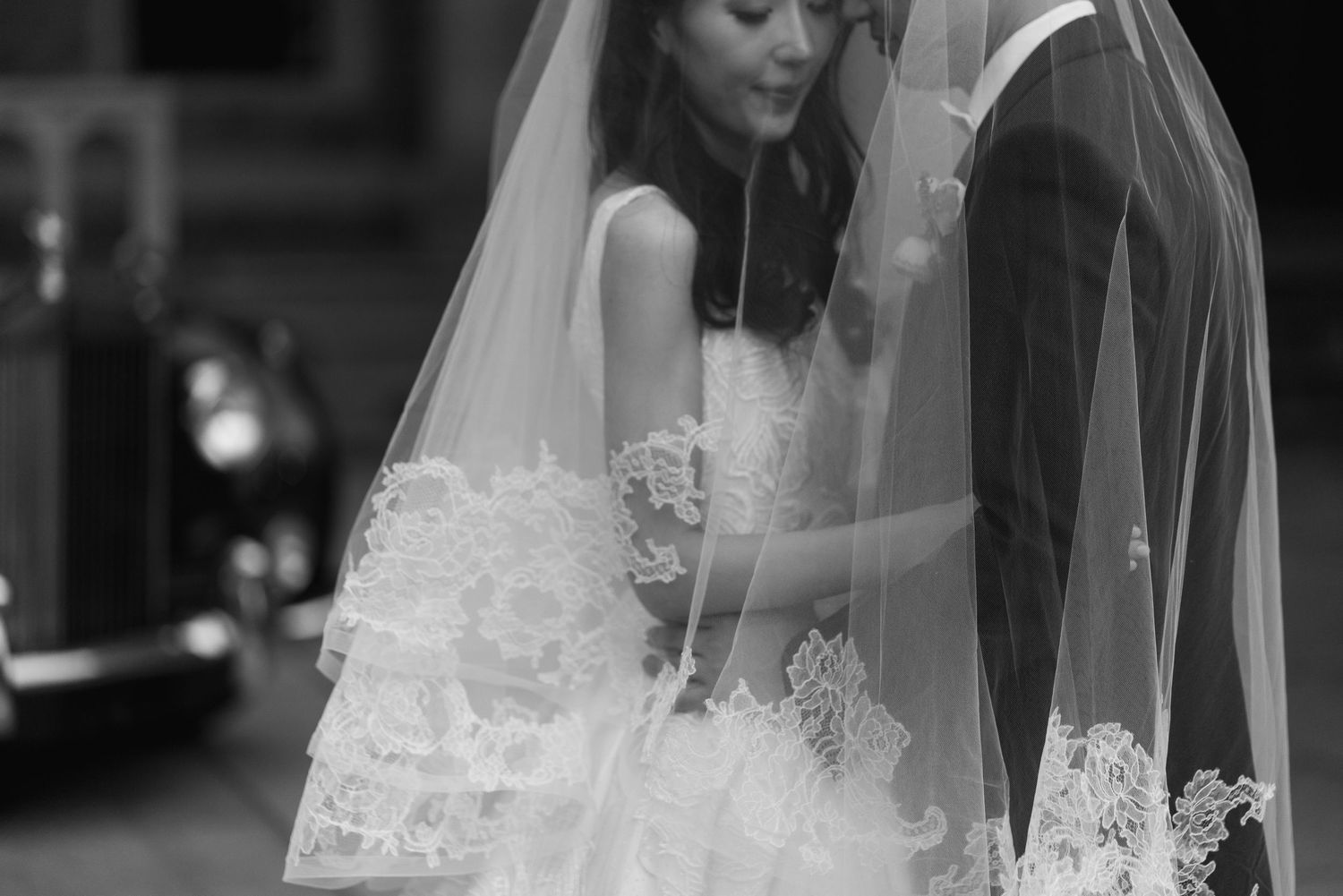 Intimate  wedding portrait of a bride and groom standing close together beneath a delicate lace-trimmed bridal veil at Casa Loma