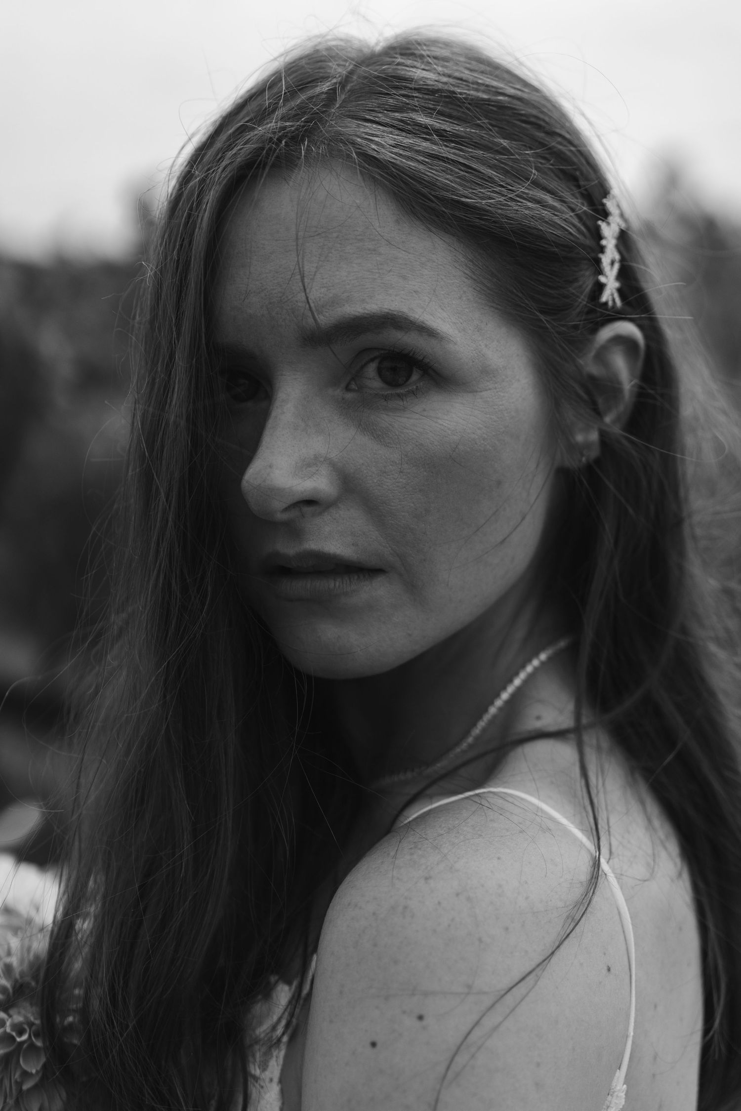 Moody black-and-white close-up portrait of a bride looking over her shoulder, with long hair and a delicate hair accessory.