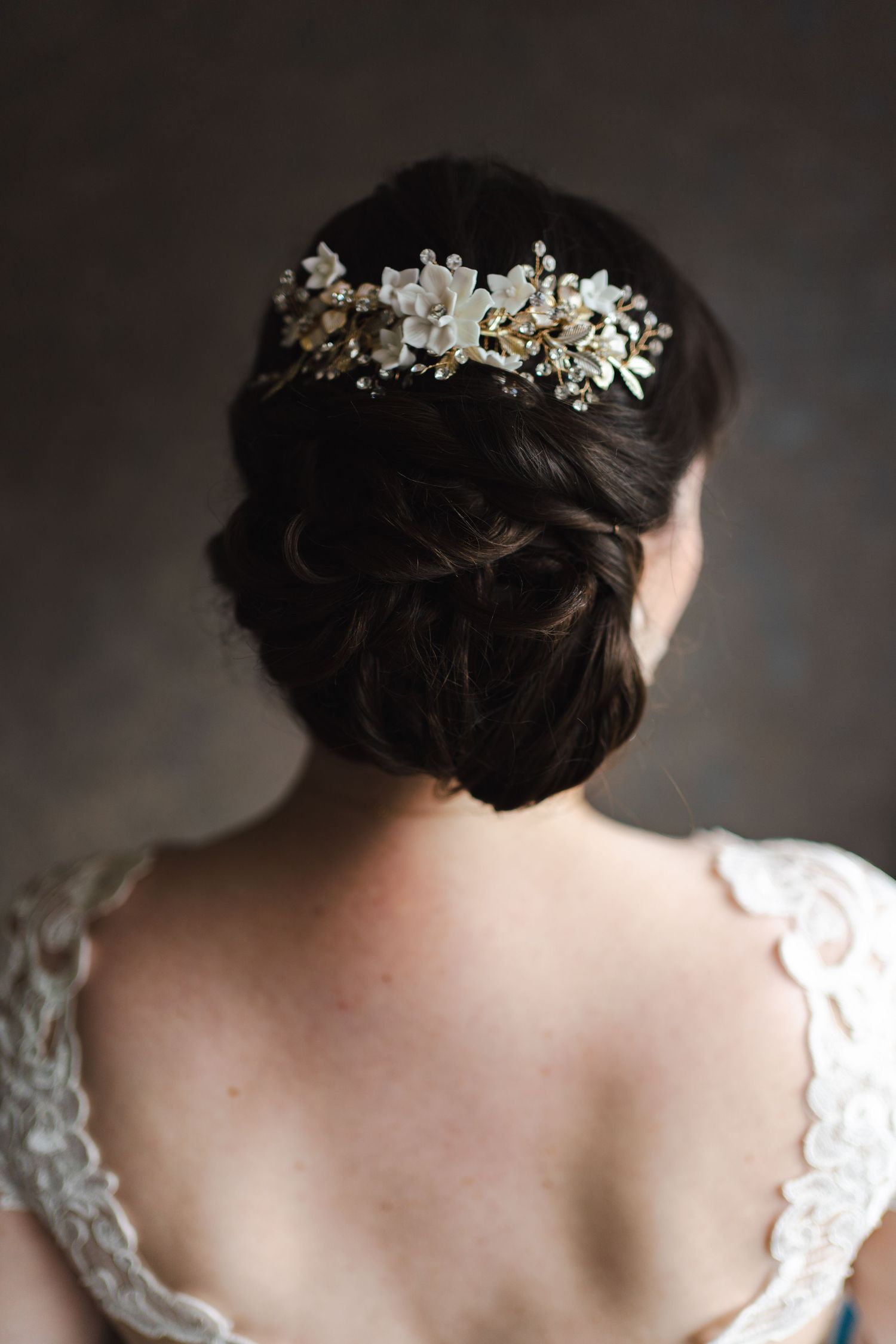 Elegant bridal hairstyle with a delicate floral hairpiece, photographed from behind to highlight the intricate updo and lace wedding dress.