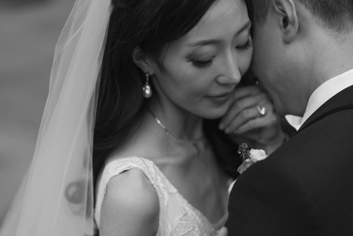 Intimate black-and-white wedding portrait of a bride and groom embracing, with the bride resting her face against the groom.