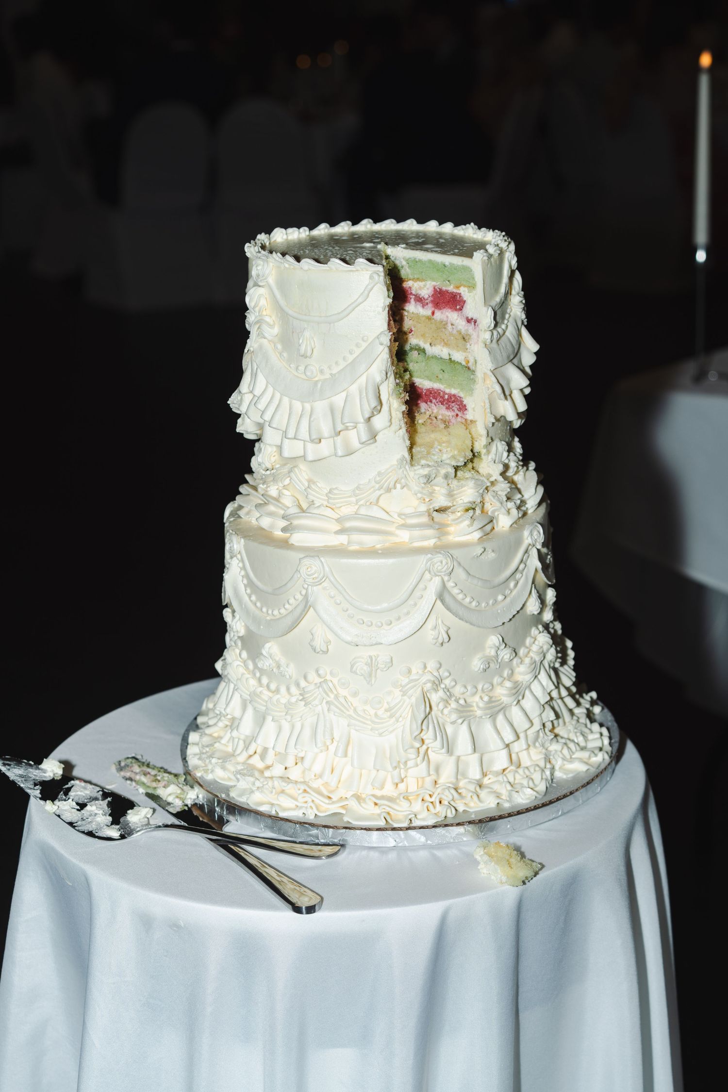 Tall white tiered wedding cake decorated with delicate floral piping and colourful accents, displayed on a small round table.