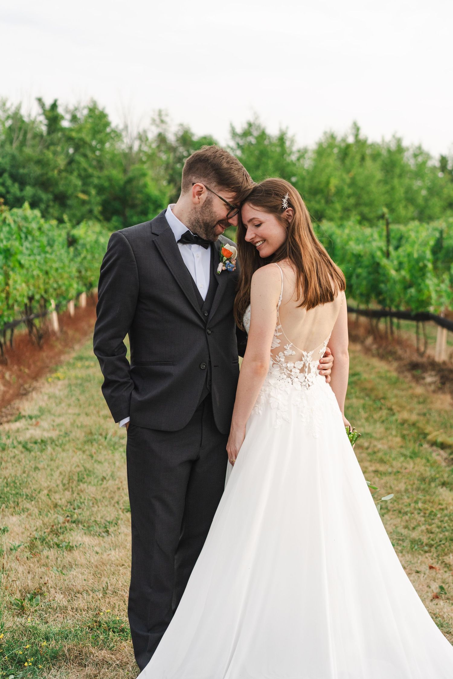 Bride and groom sharing a tender moment on a vineyard path surrounded by green grapevines at Calamus Estate Winery in Jordan, Ontario.