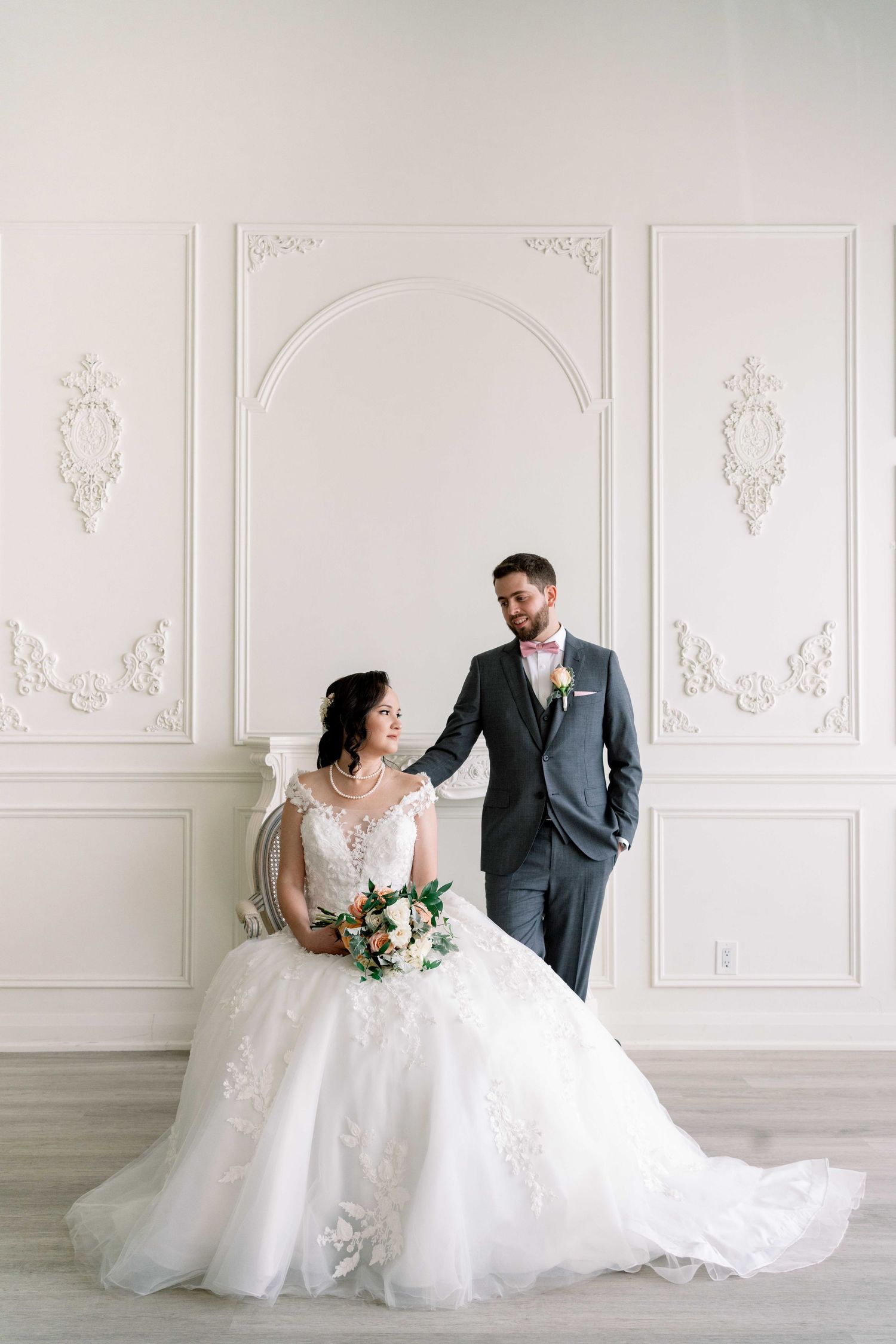 Bride in a flowing white wedding gown seated beside the groom in an elegant white studio setting at ESpace Studios.