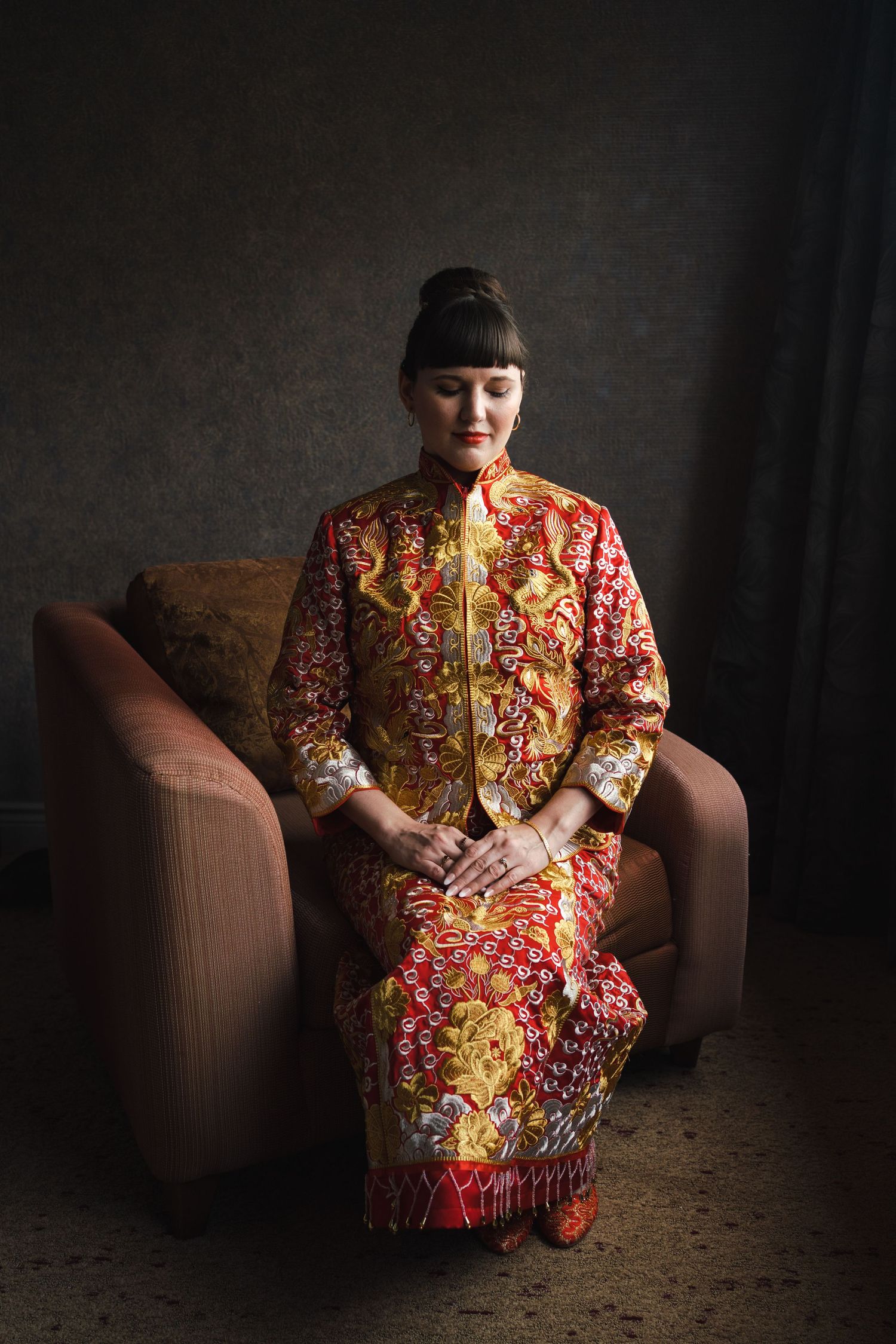 Bride seated in a softly lit room wearing an ornate red and gold traditional Chinese wedding outfit at the Westin Hotel