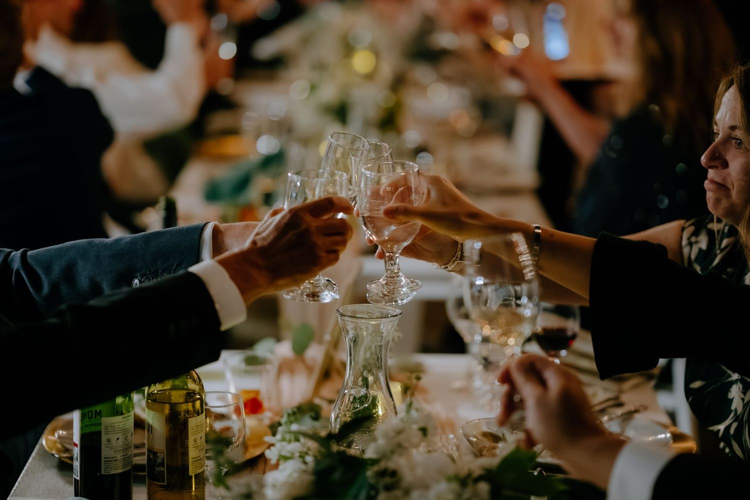 Wedding guests clinking champagne glasses in a toast at an elegant reception dinner table.