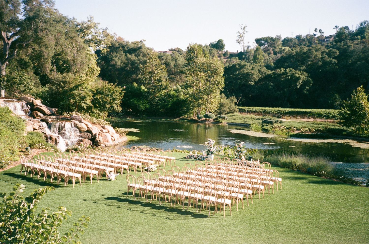 Outdoor wedding ceremony setup with rows of chairs beside a serene garden pond.