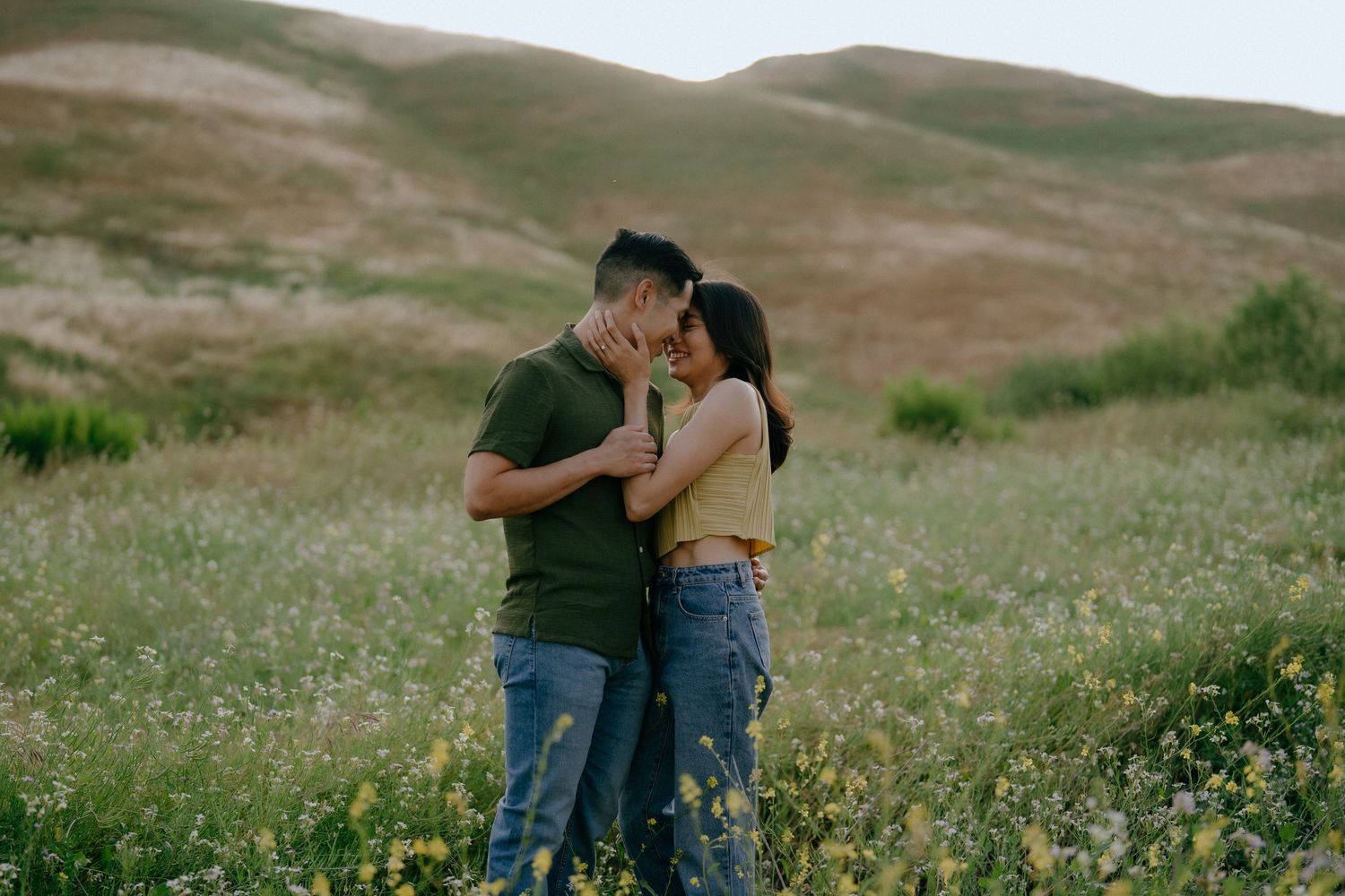 Couple embracing romantically in a wildflower meadow with rolling green hills in the background.