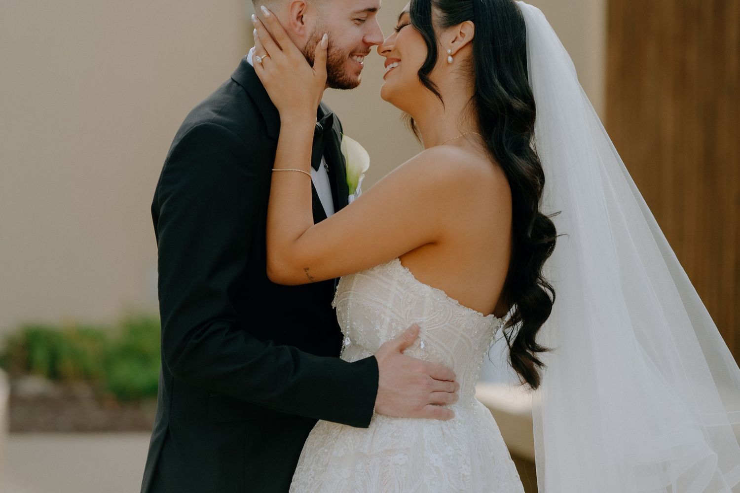 Smiling bride and groom share a romantic moment in wedding attire outdoors.