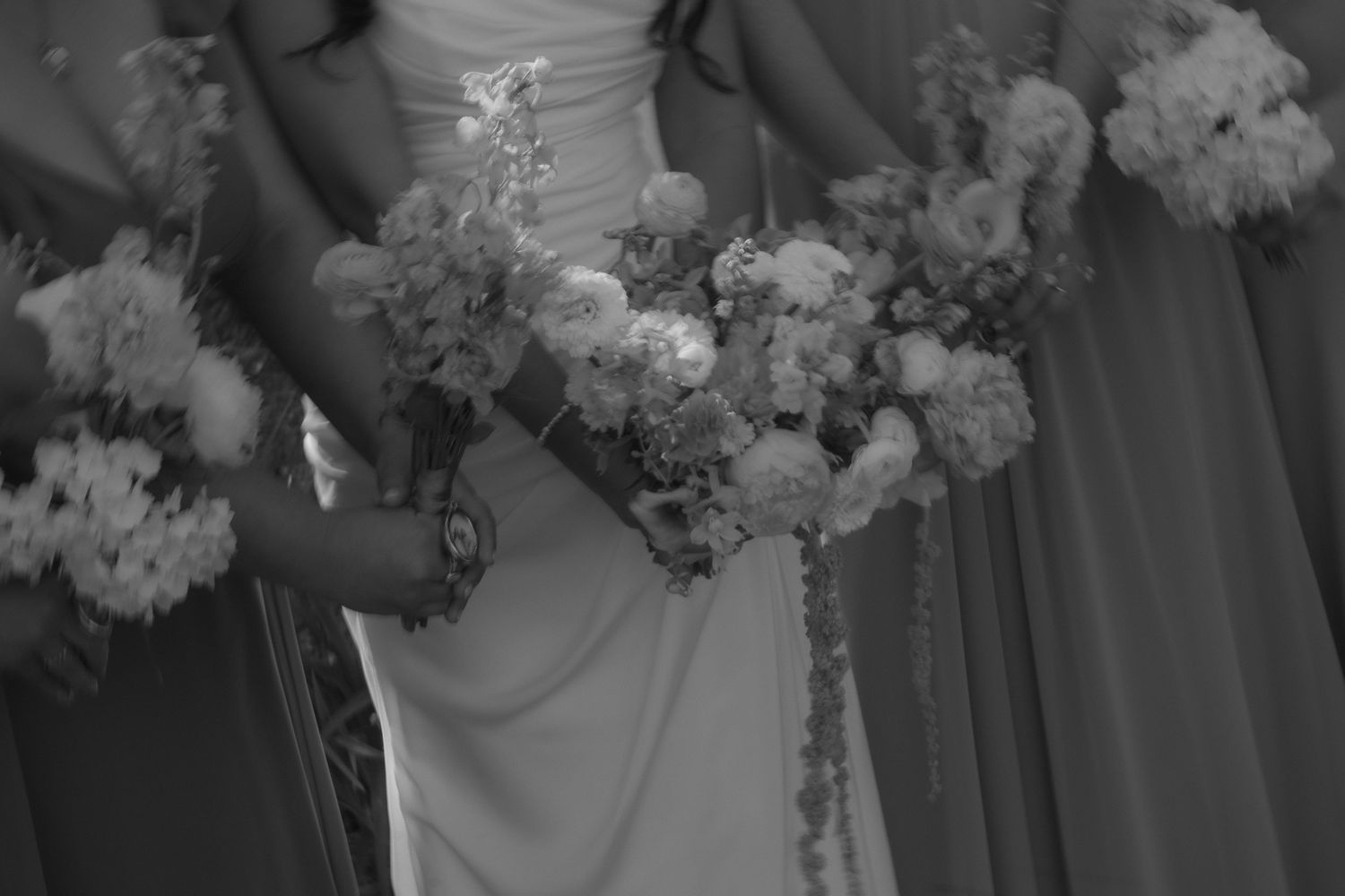 Black and white photo of bridesmaids holding floral bouquets in elegant dresses.