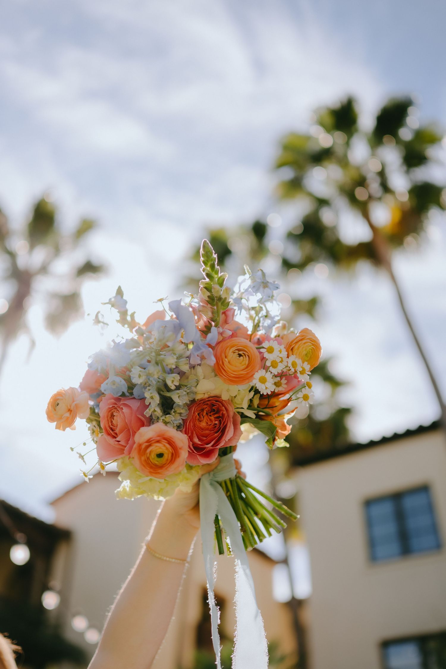 Vibrant bridal bouquet of orange ranunculus and white flowers held against blue sky.
