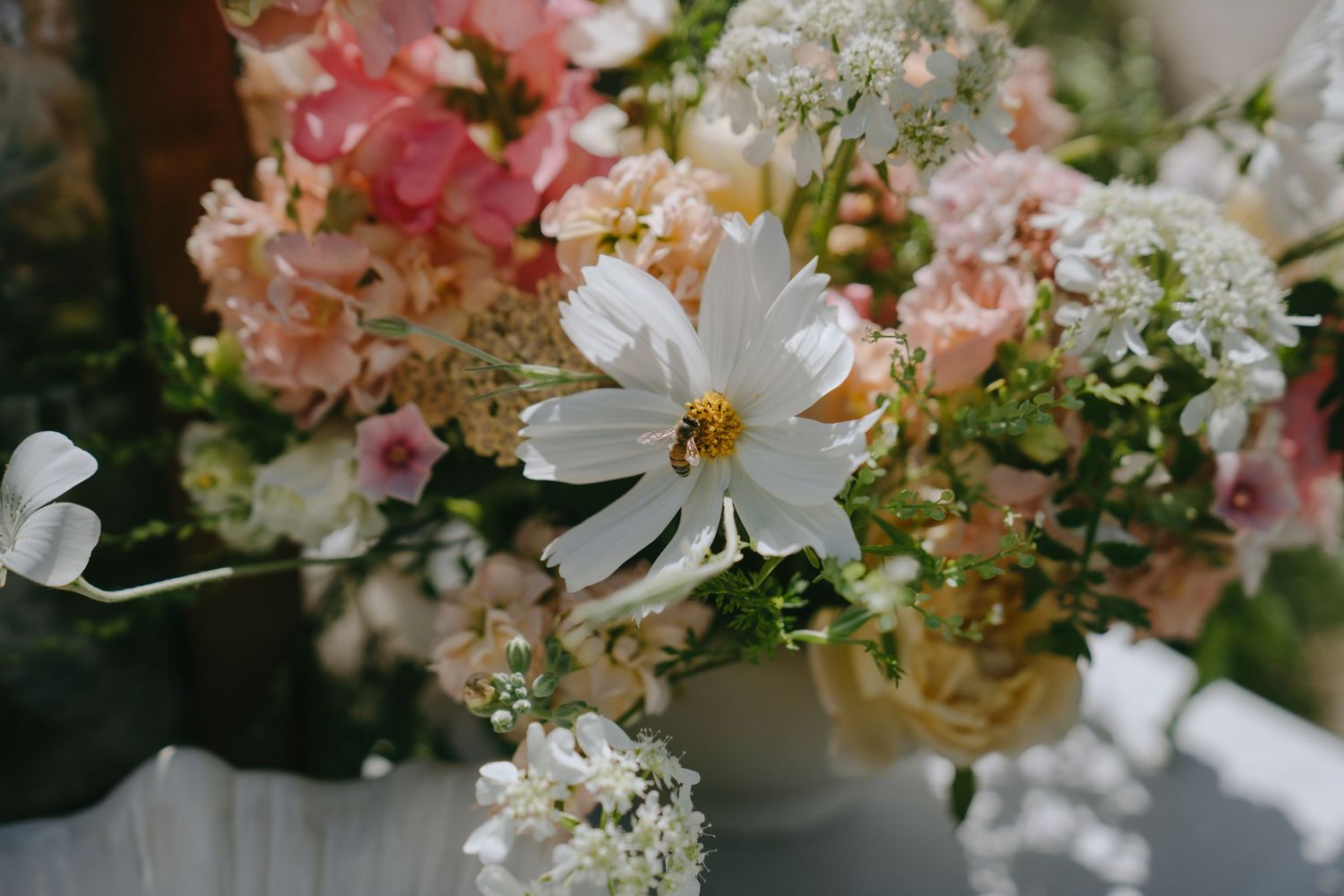 Close-up of a beautiful floral arrangement featuring white cosmos, pink hydrangeas, and delicate wildflowers in soft natural light.