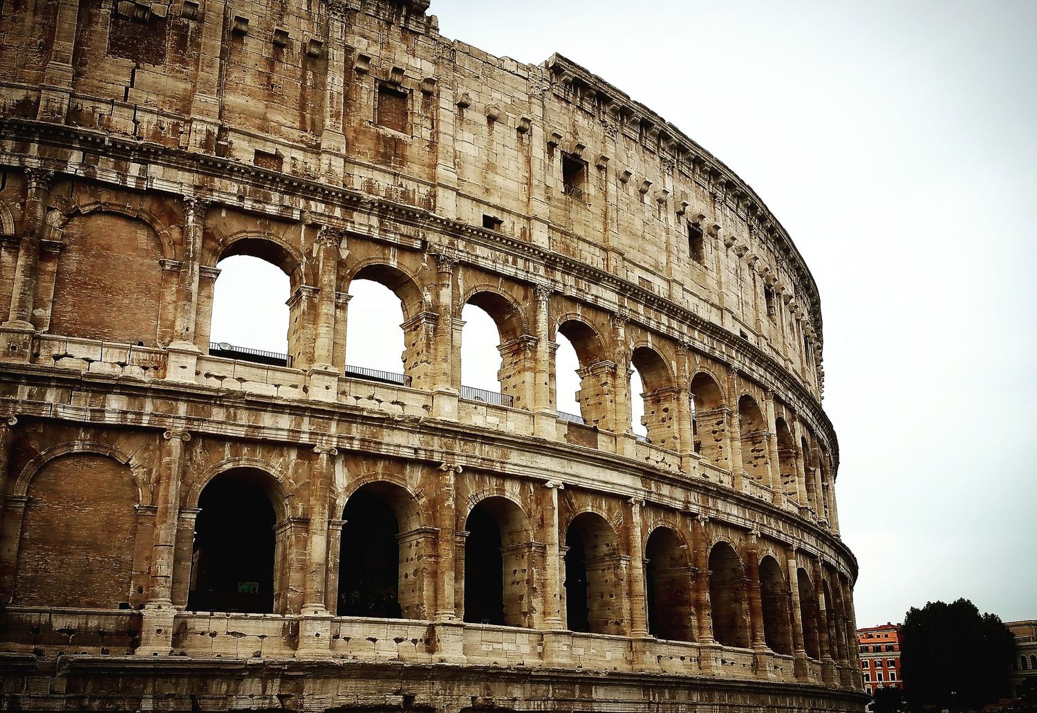Ancient Roman Colosseum exterior with weathered stone arches rising under a soft gray sky.