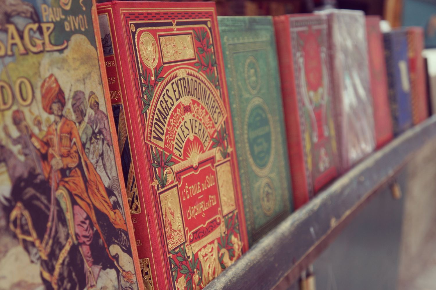 Antique decorative hardcover books with vivid red and green gilded covers line a shelf at a vintage book market.