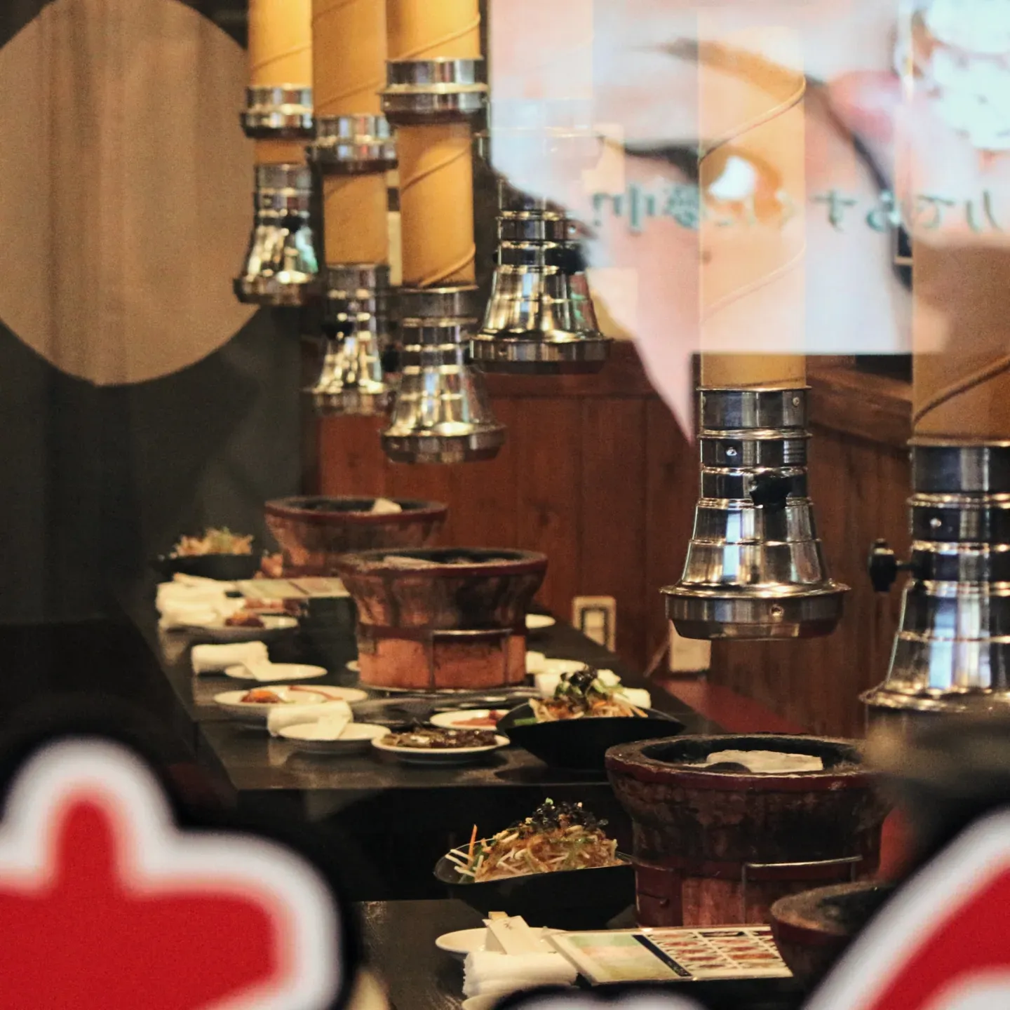Japanese yakiniku restaurant interior with tabletop grills, metal exhaust hoods and plates of food ready for dining.